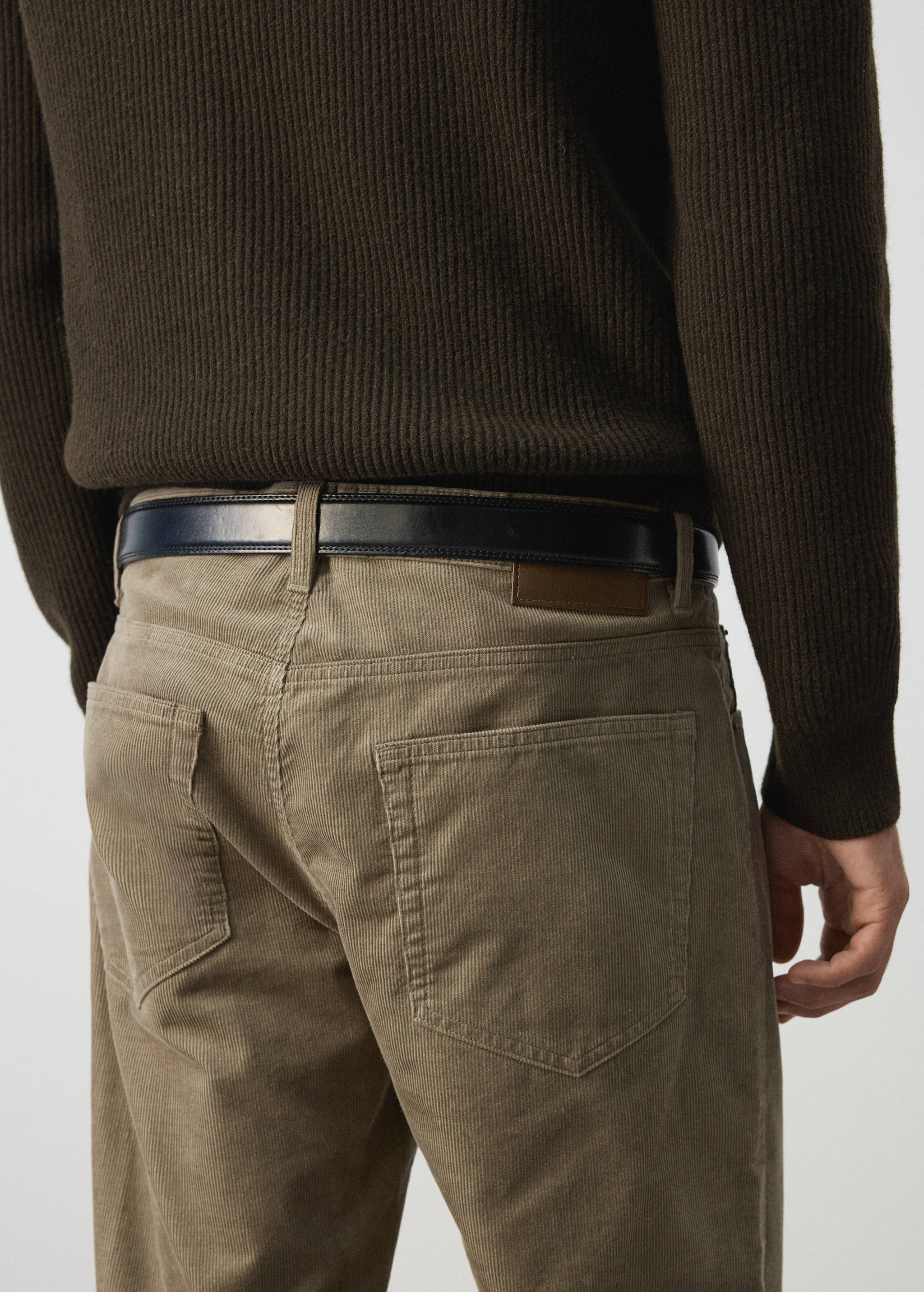 Beige corduroy trousers with back patch pockets, worn with a dark belt.