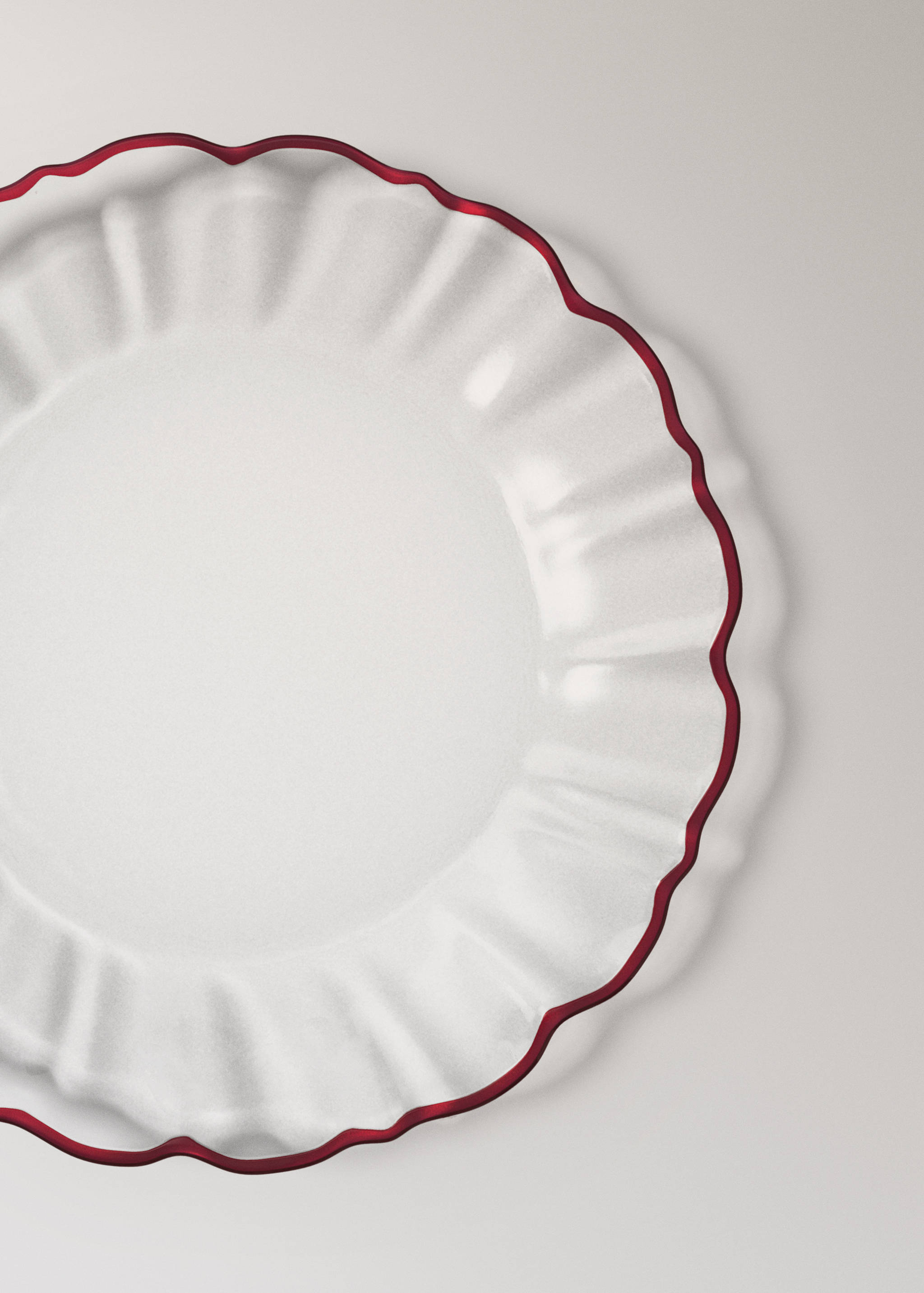 Round glass plate with a fluted rim and red scalloped border.
