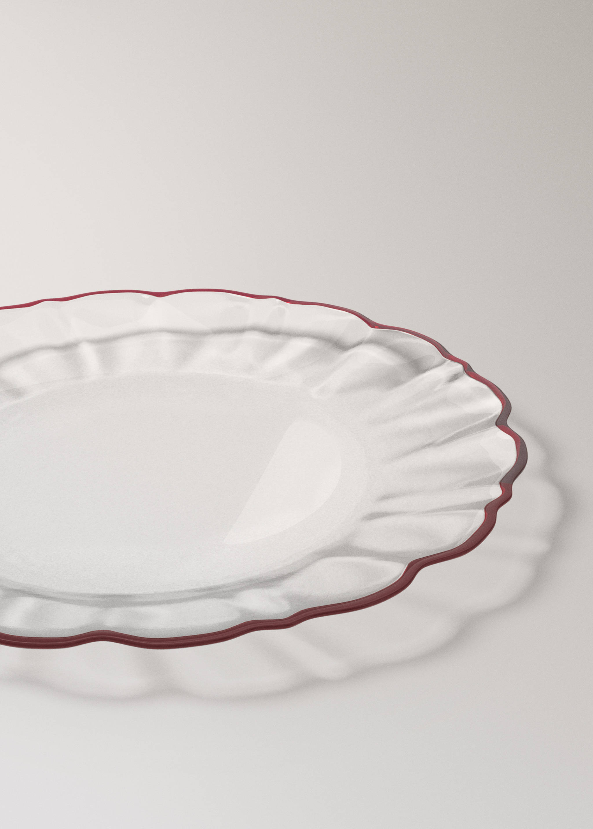 Clear glass plate with a fluted rim and dark red scalloped edge.
