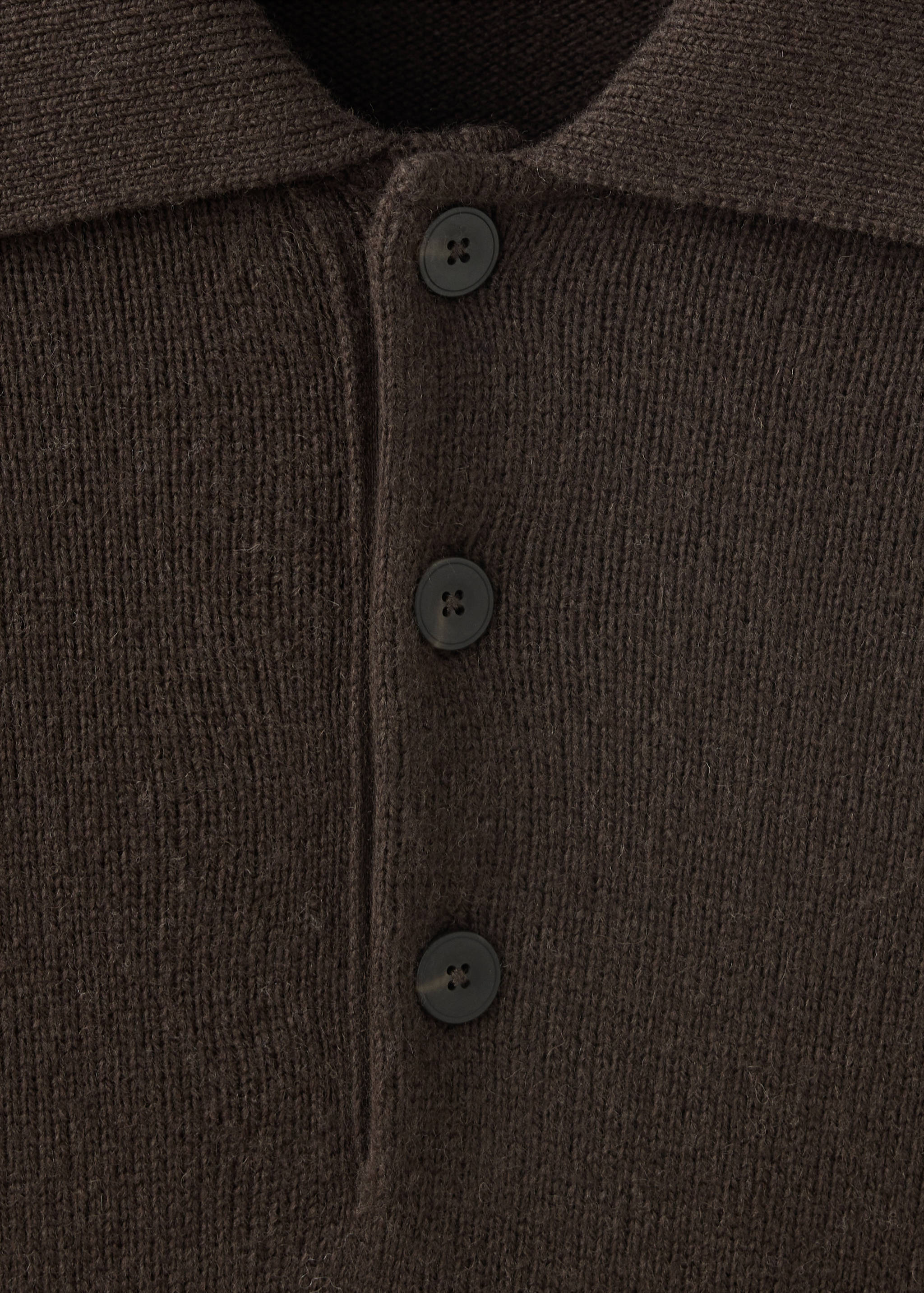 Primer plano de un polo de punto en marrón oscuro con tapeta de botones.