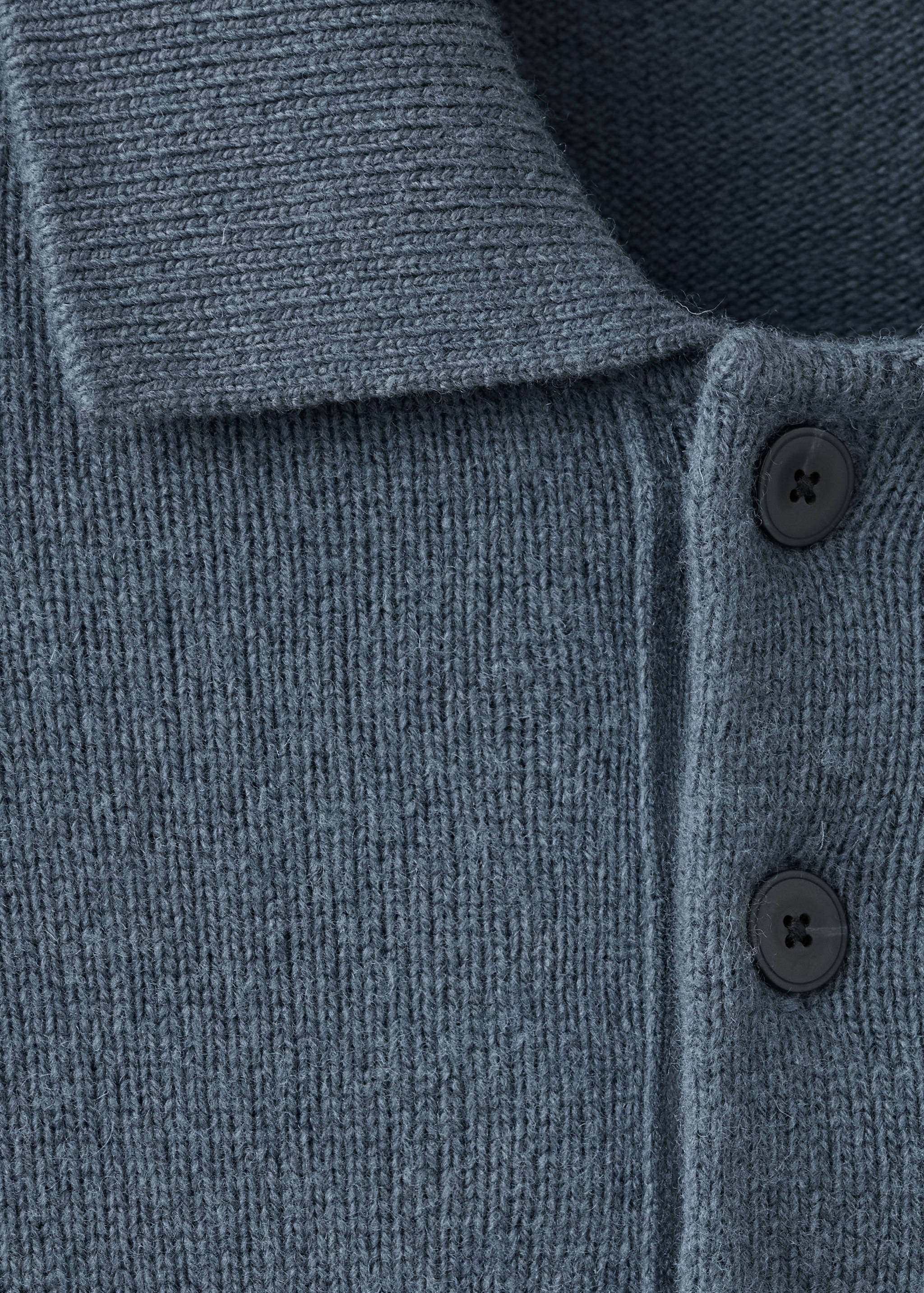 Primer plano del cuello y la plaqueta de botones de un polo de punto en gris azulado oscuro.