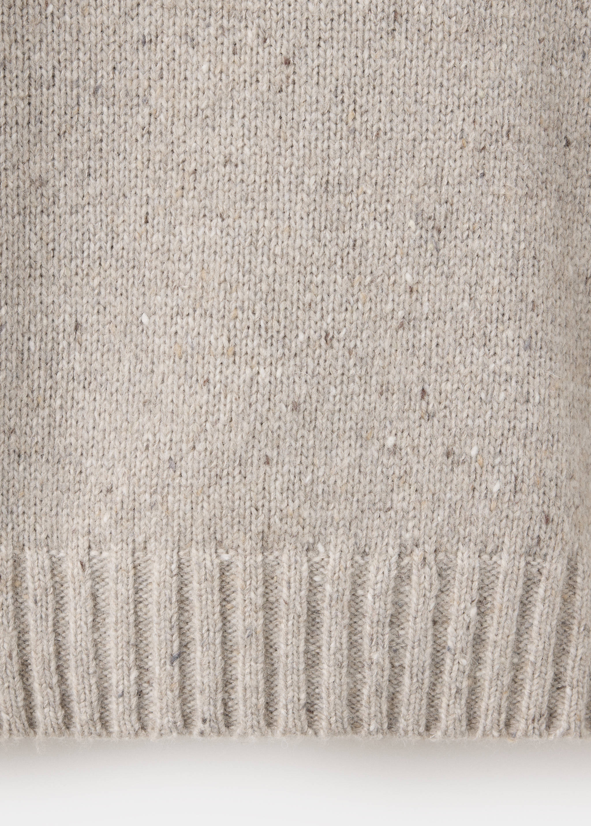 Close-up of a beige speckled knit sweater with a ribbed hem.