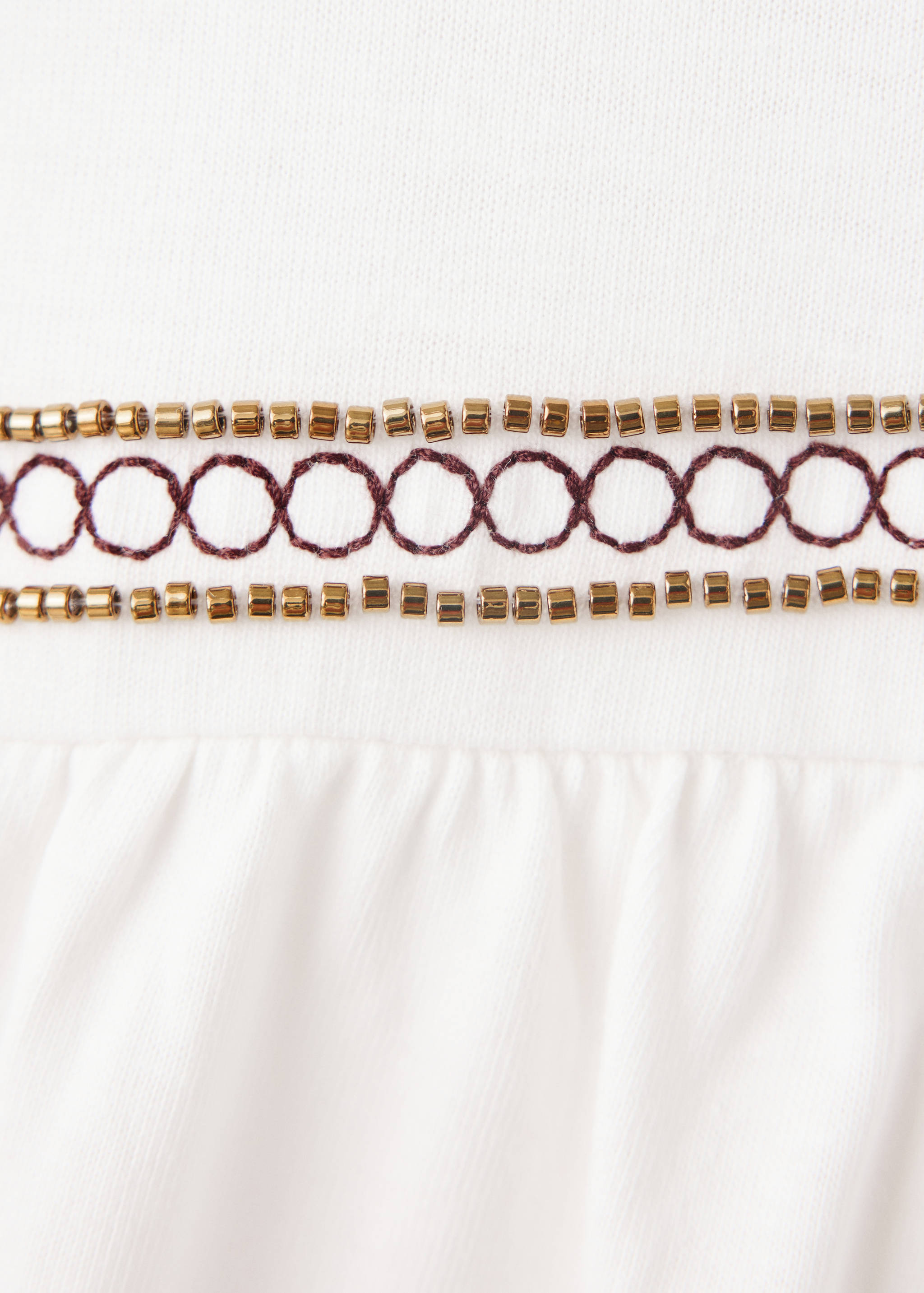 Close-up of a white T-shirt with beaded and embroidered trim.