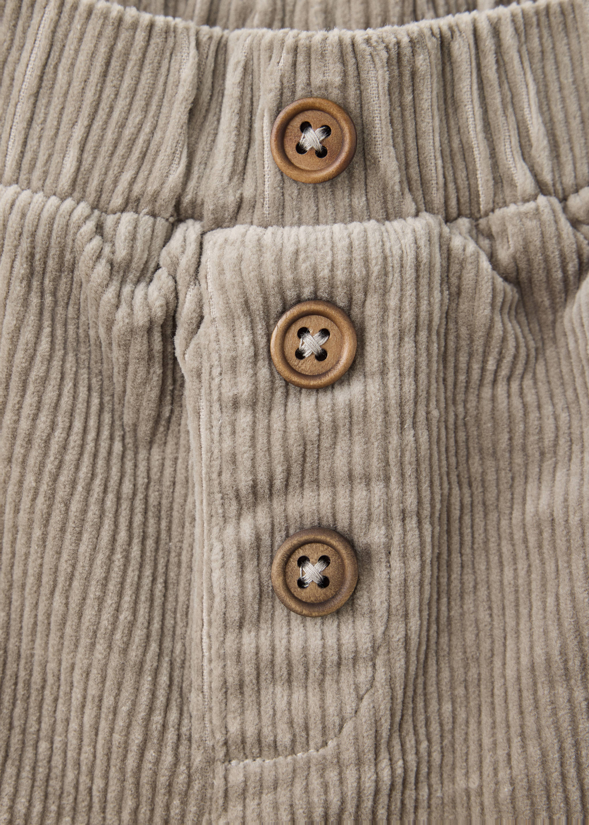 Close-up of beige corduroy trousers featuring a button-front placket and wooden buttons.