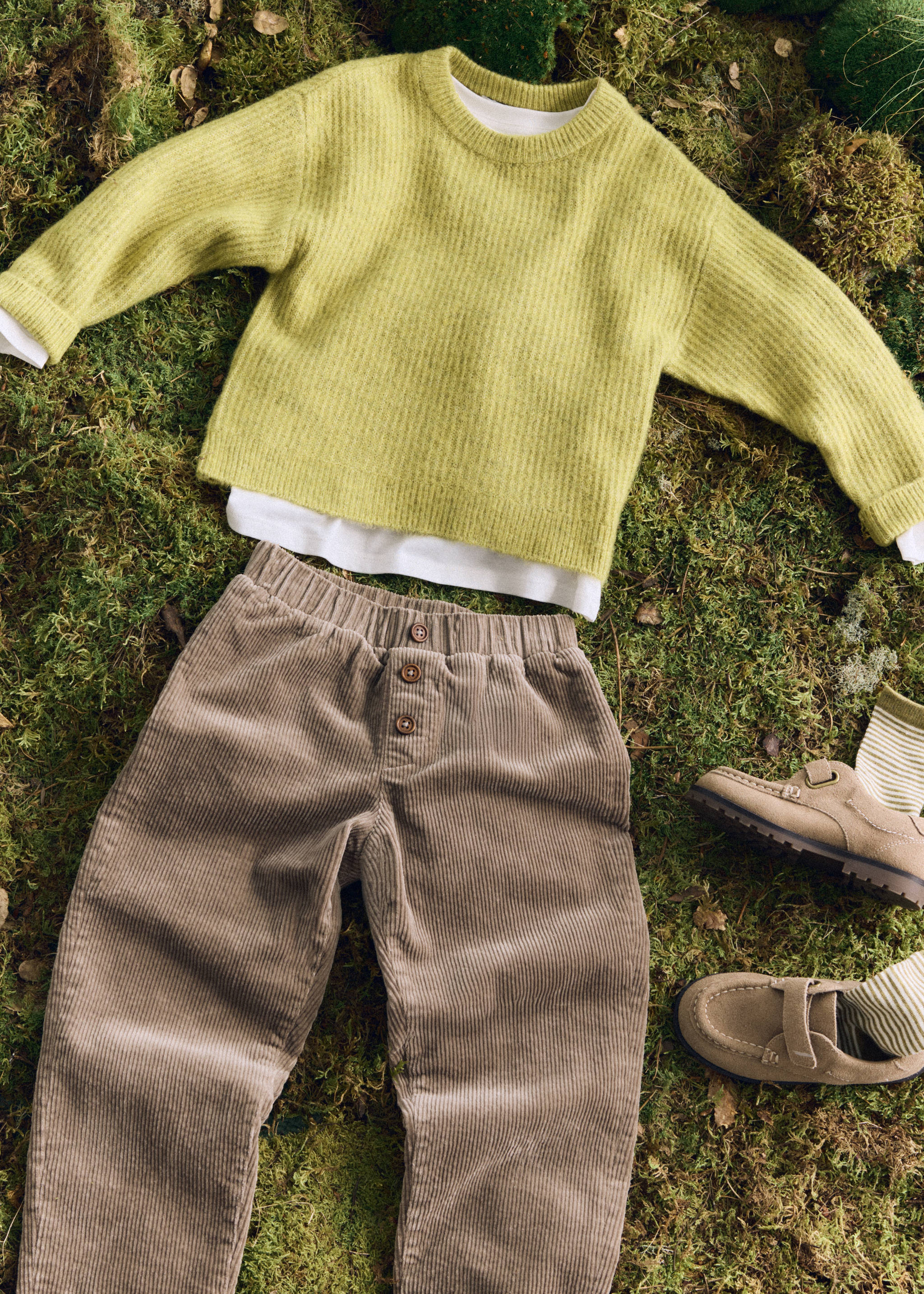 Brown corduroy trousers with an elasticated waistband and front buttons on a mossy ground.