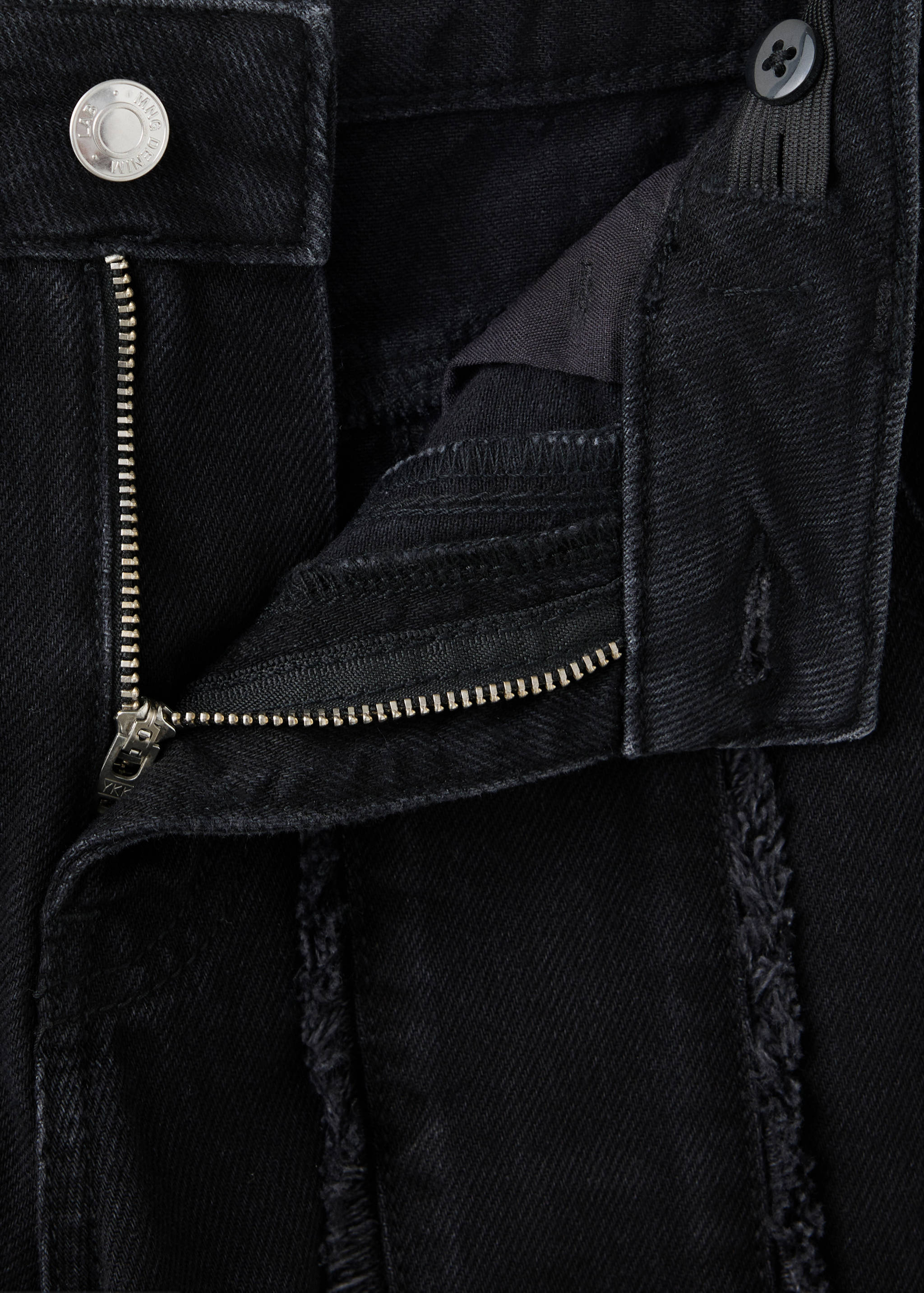 Black denim trousers fabric detail showcasing the zip fly and frayed seams