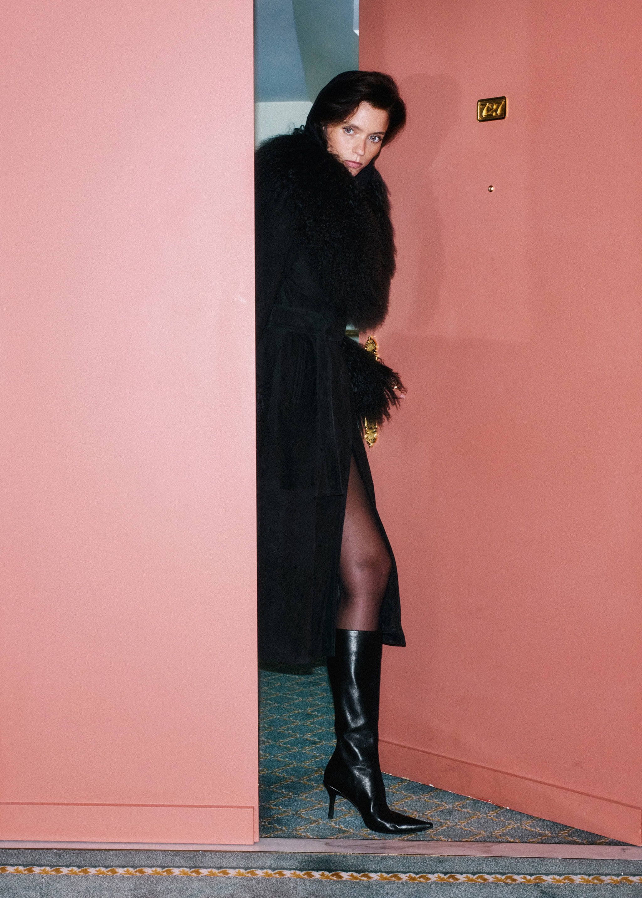Black leather heeled boots with pointed toes worn by a model in a doorway.