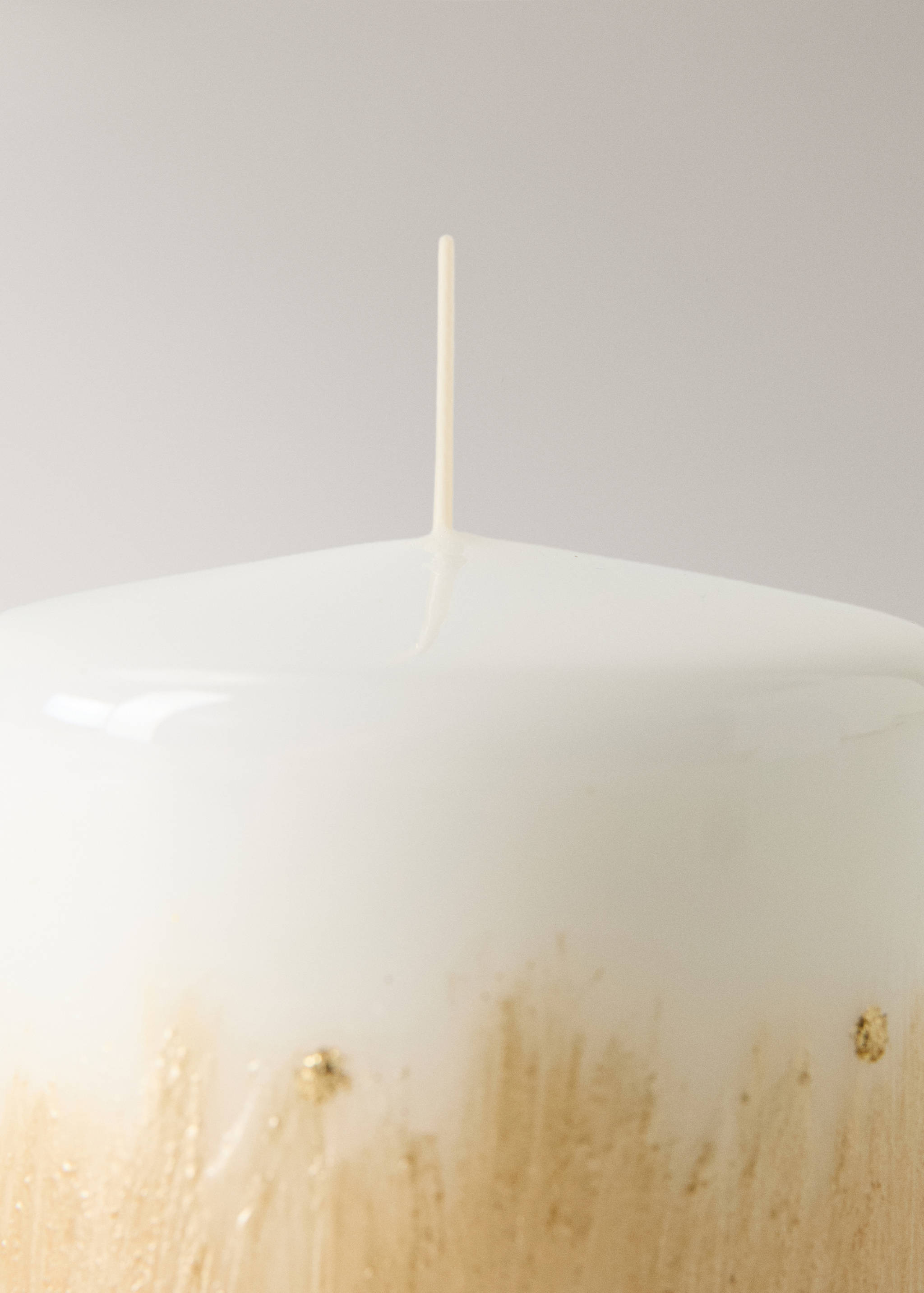 Close-up of a white candle with a gold metallic textured base.