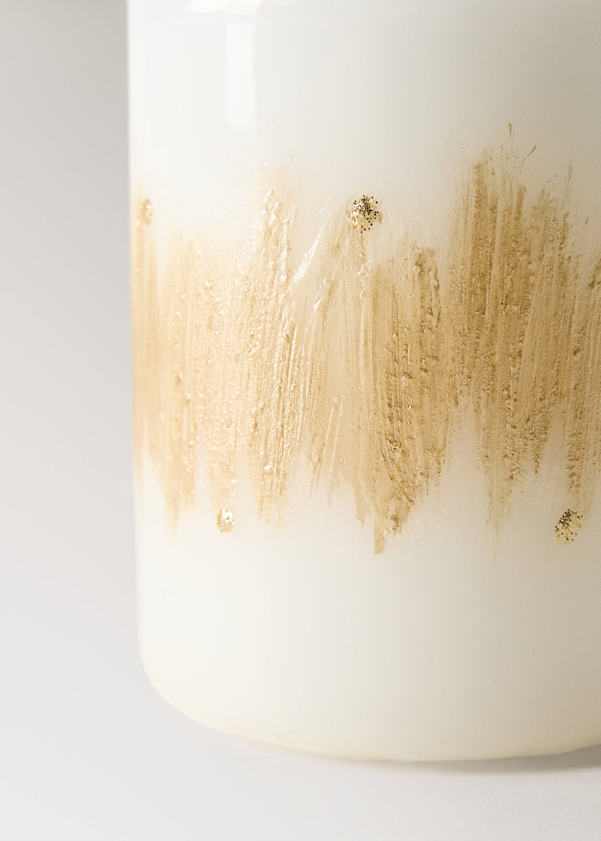 Close-up of a white candle with a gold-painted textured band and glitter.