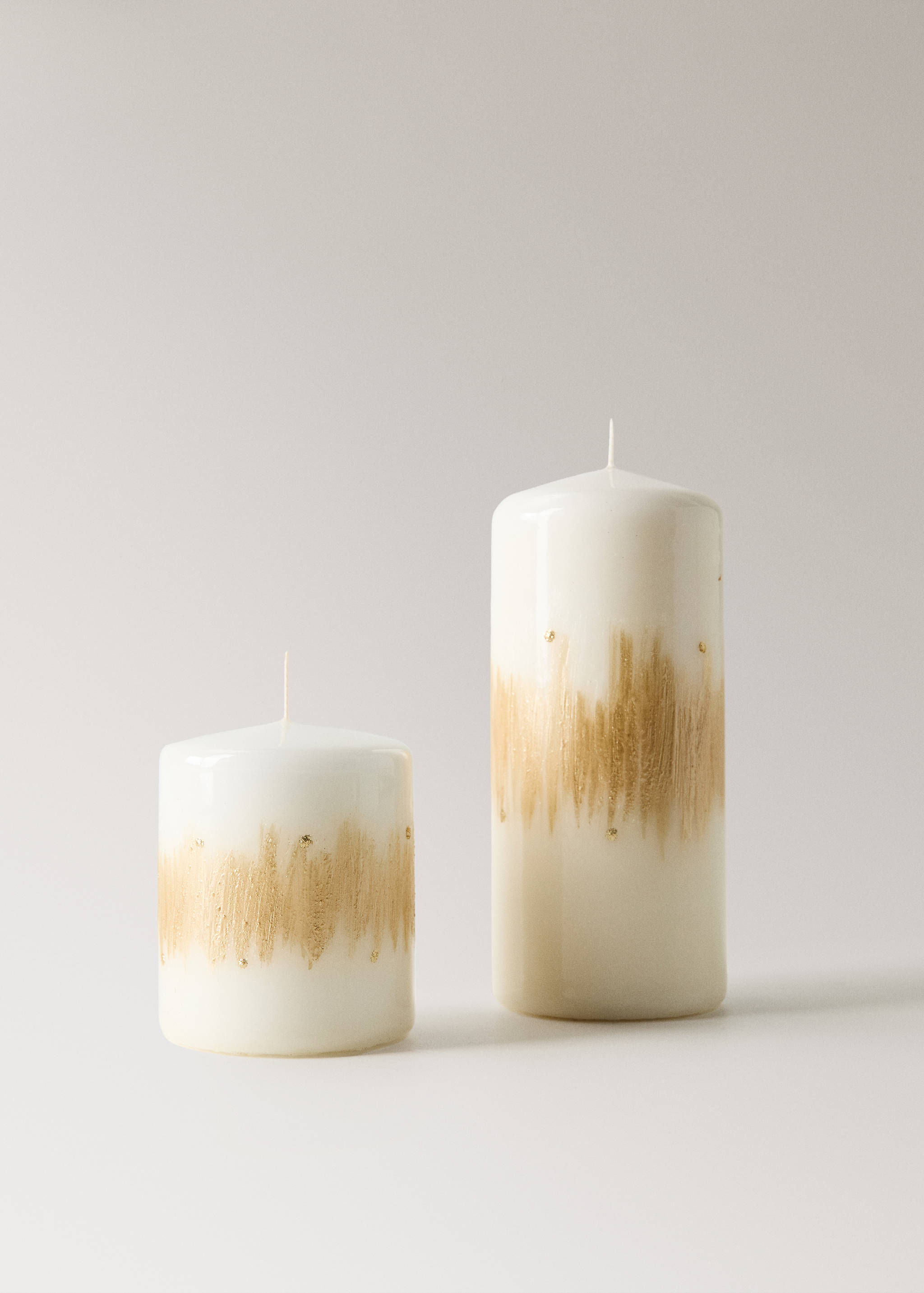 Two white pillar candles with brushed gold detail.