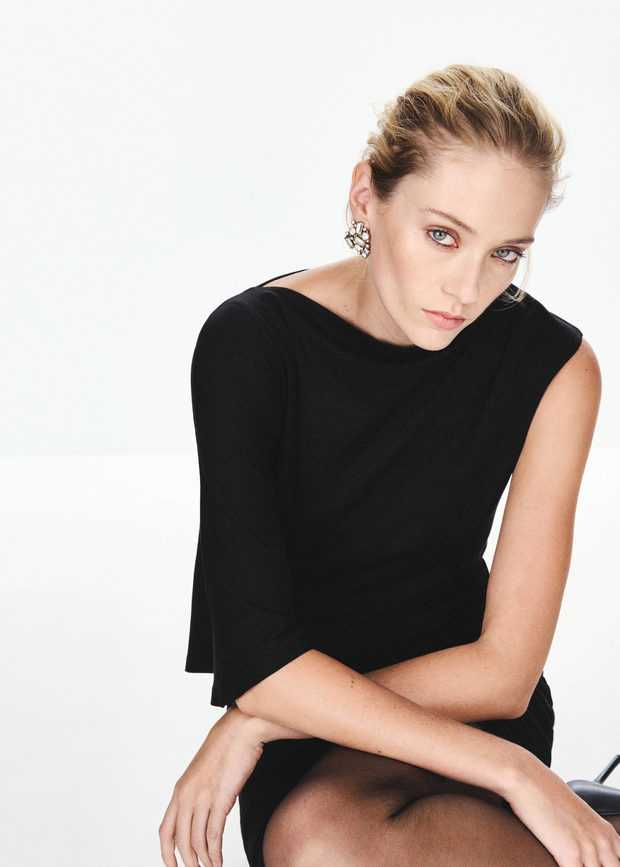 Black dress with a boat neckline and short sleeves, featured in a close-up portrait with crystal earrings.