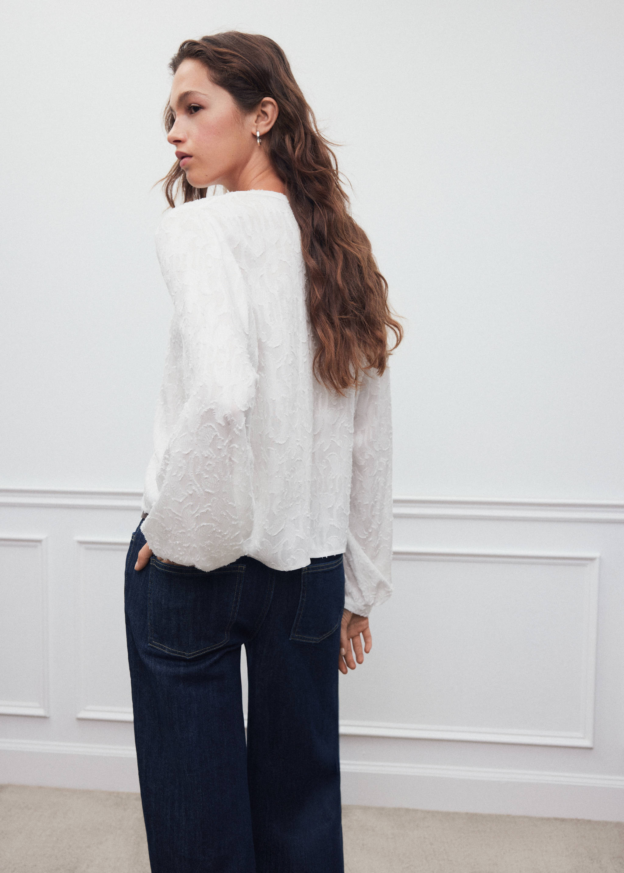 White textured long-sleeve blouse, back view, paired with dark blue denim trousers.