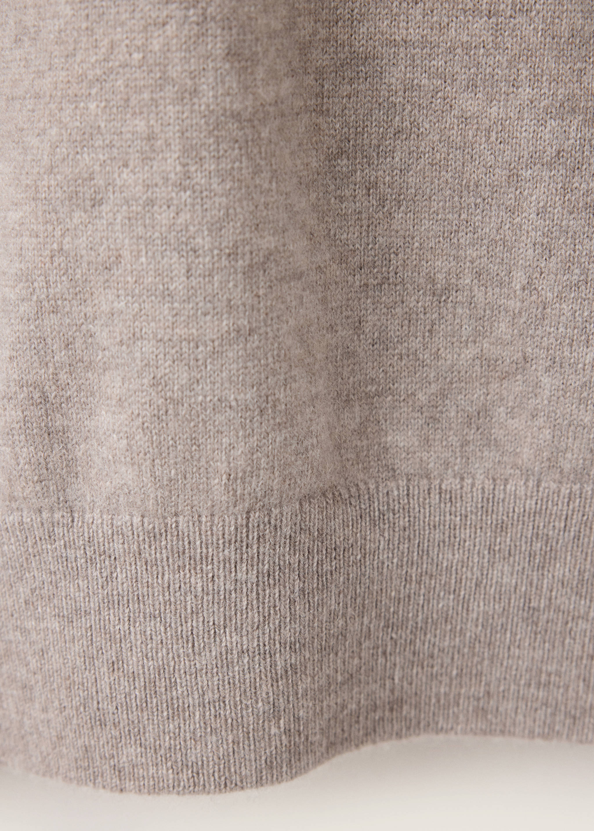 Close-up of a light beige knitted jersey showing texture and ribbed hem.