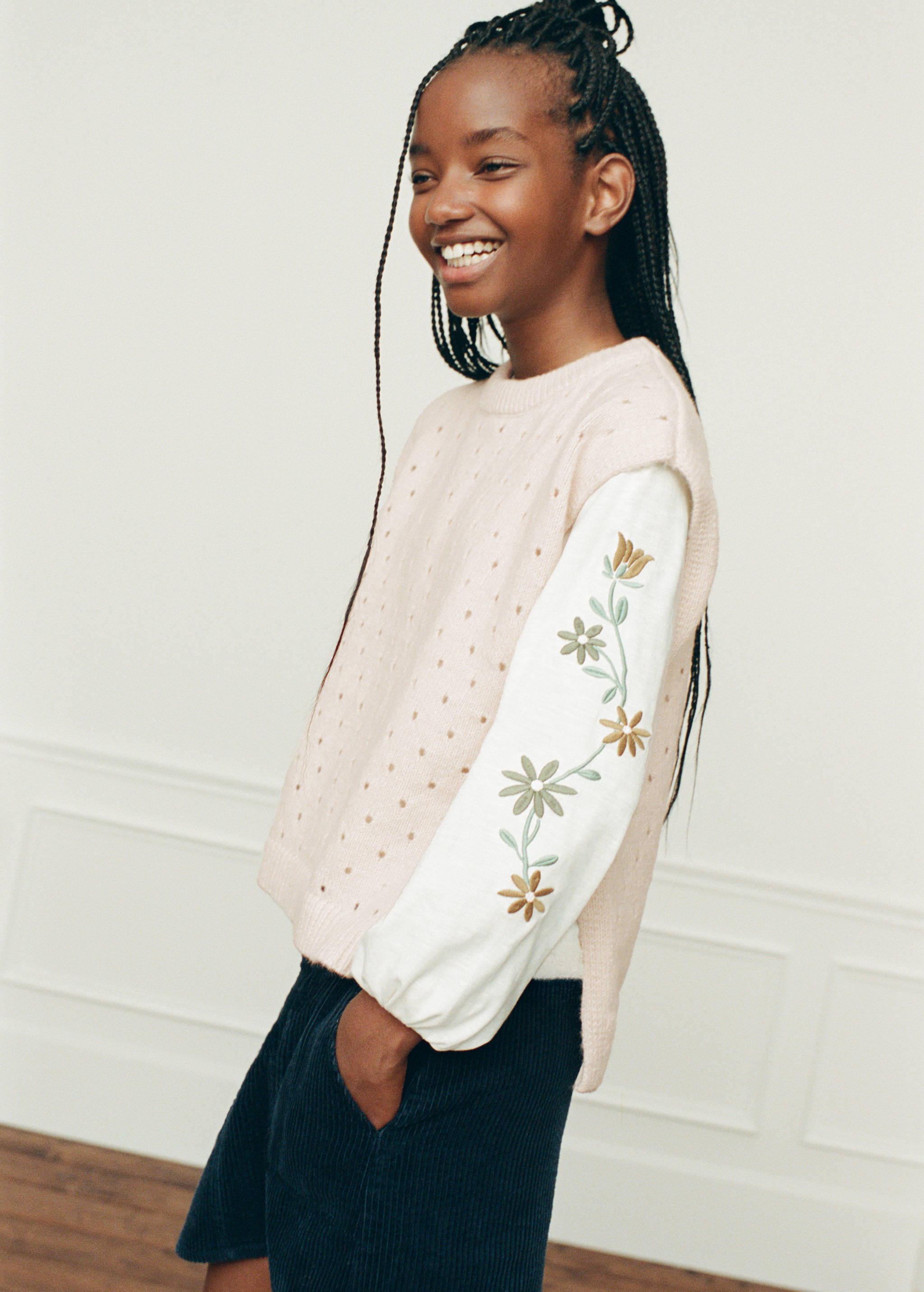White long-sleeved t-shirt with embroidered floral sleeve details, worn layered under a pink knit vest.