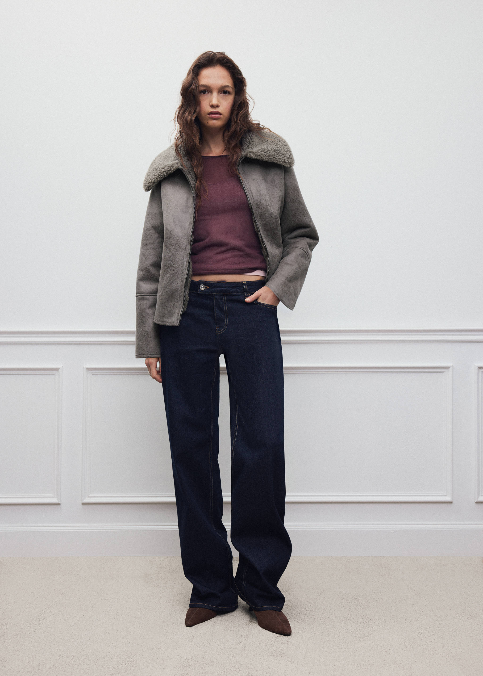 Grey faux-suede coat with faux-shearling collar worn with a dark top and blue trousers.
