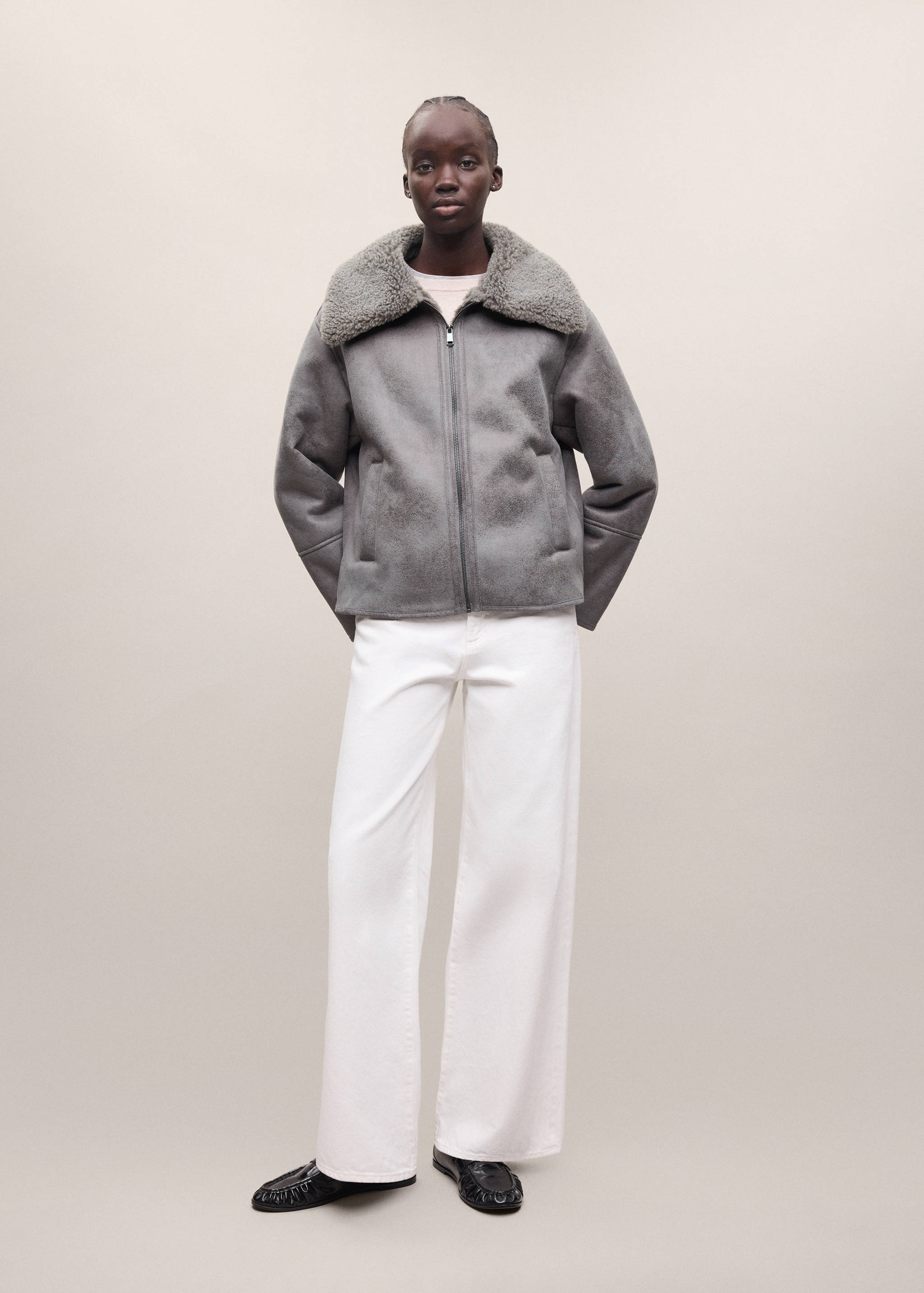 Grey faux-shearling coat with a wide collar and zip fastening, worn with white trousers.