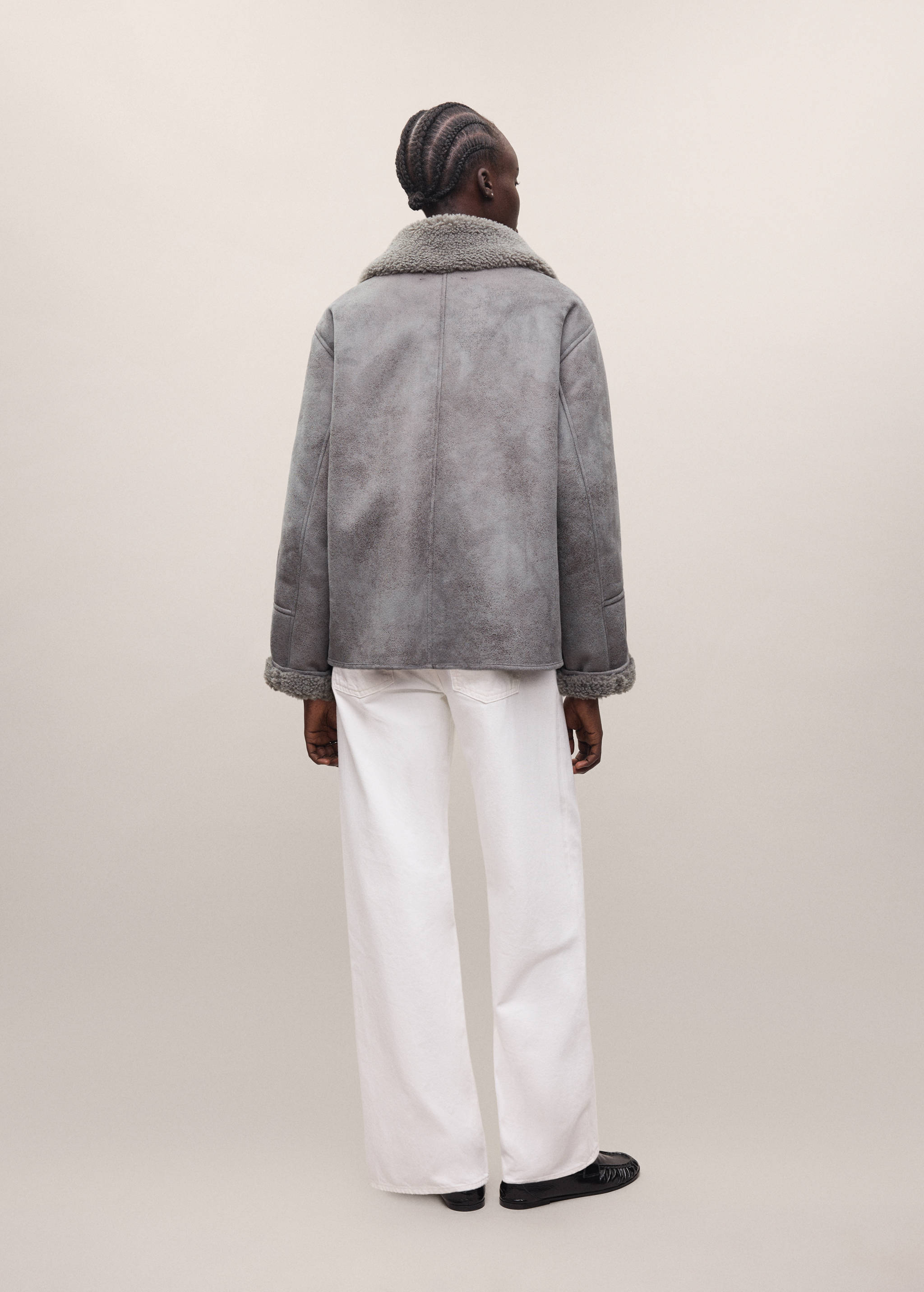 Grey faux-shearling coat shown from the back, paired with white trousers.