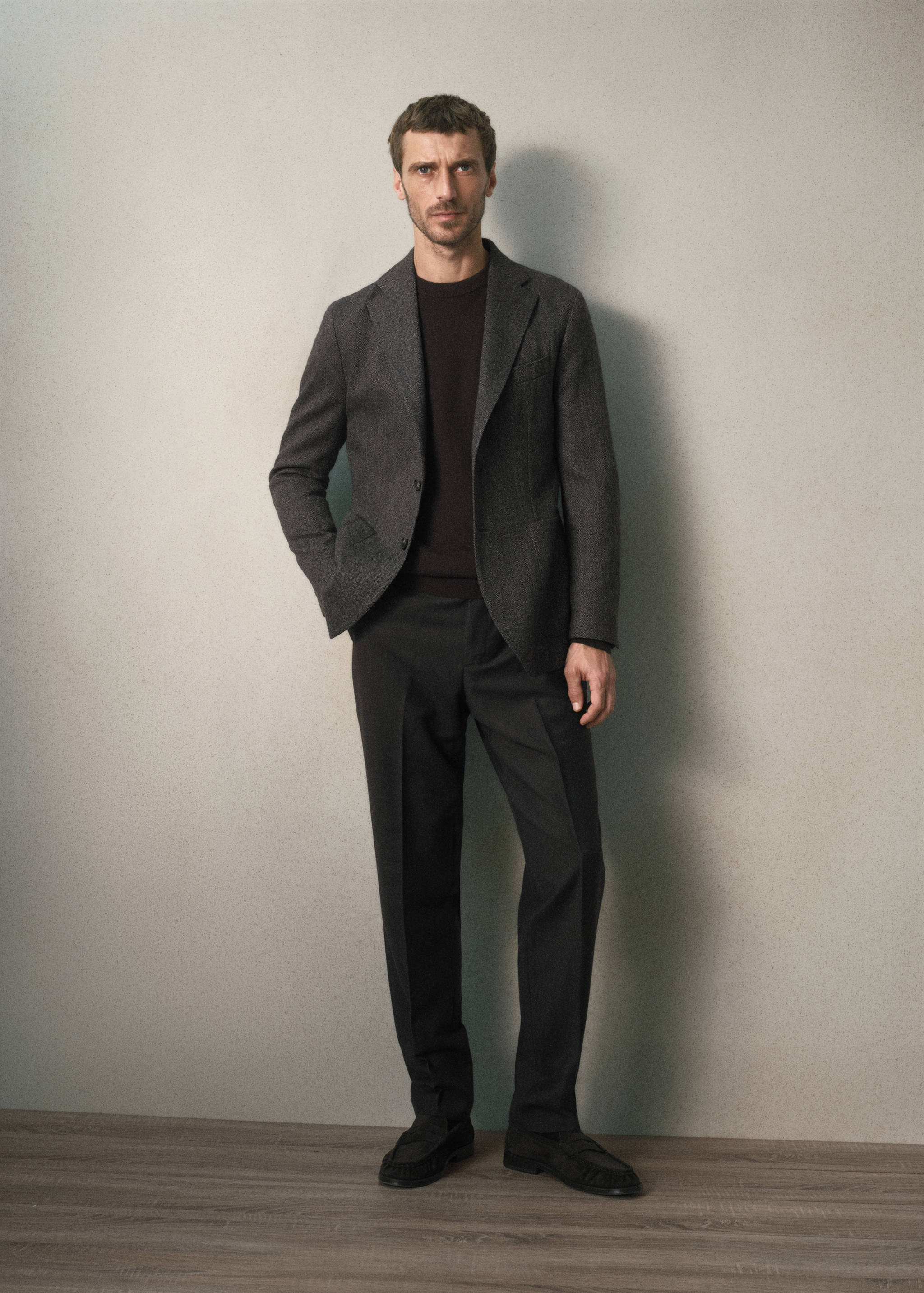 Dark grey blazer worn with a dark sweater and trousers.
