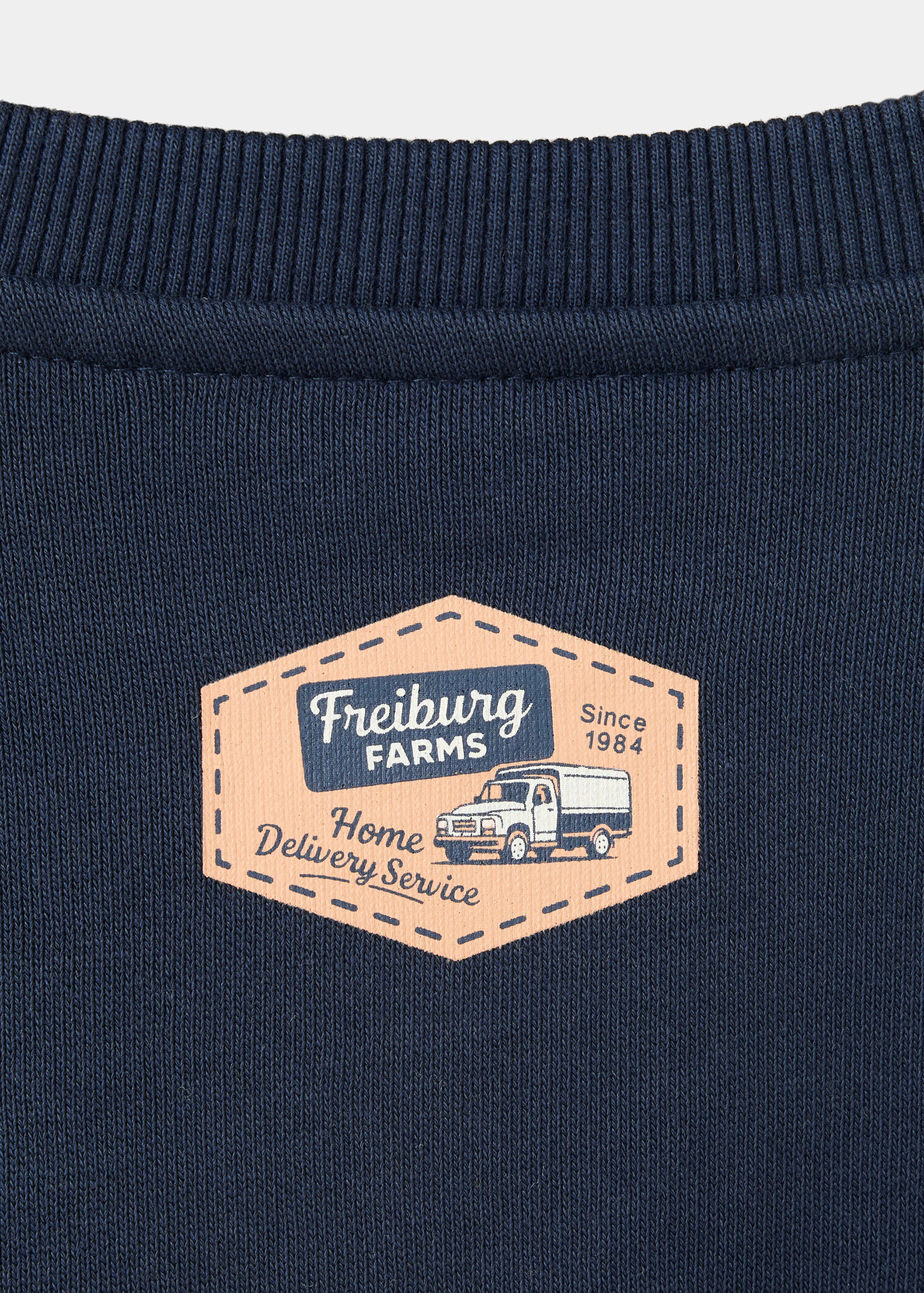 Navy blue kids sweatshirt neckline detail with a peach graphic badge.