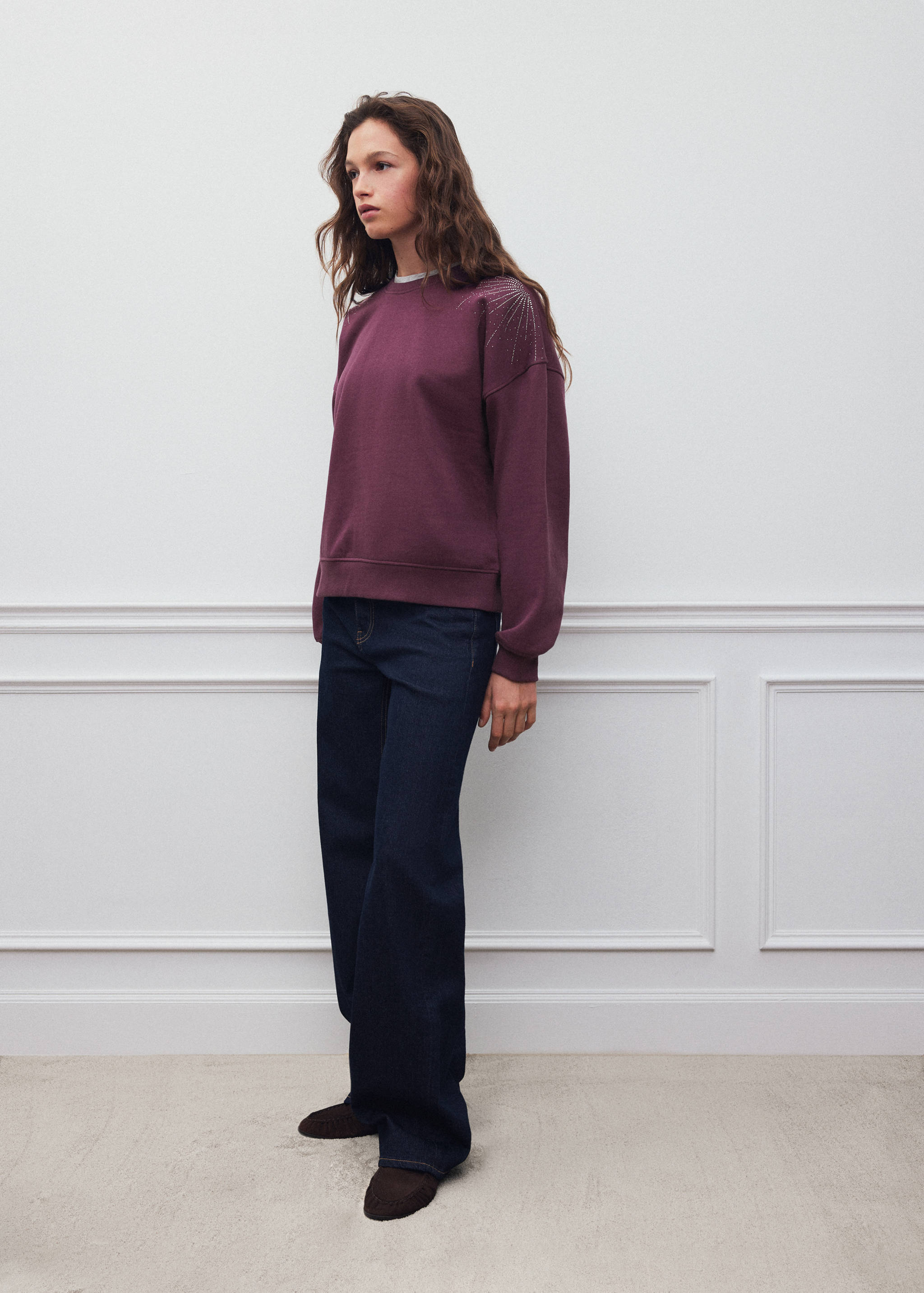 Plum sweatshirt with rhinestone shoulder detail, worn with dark trousers.