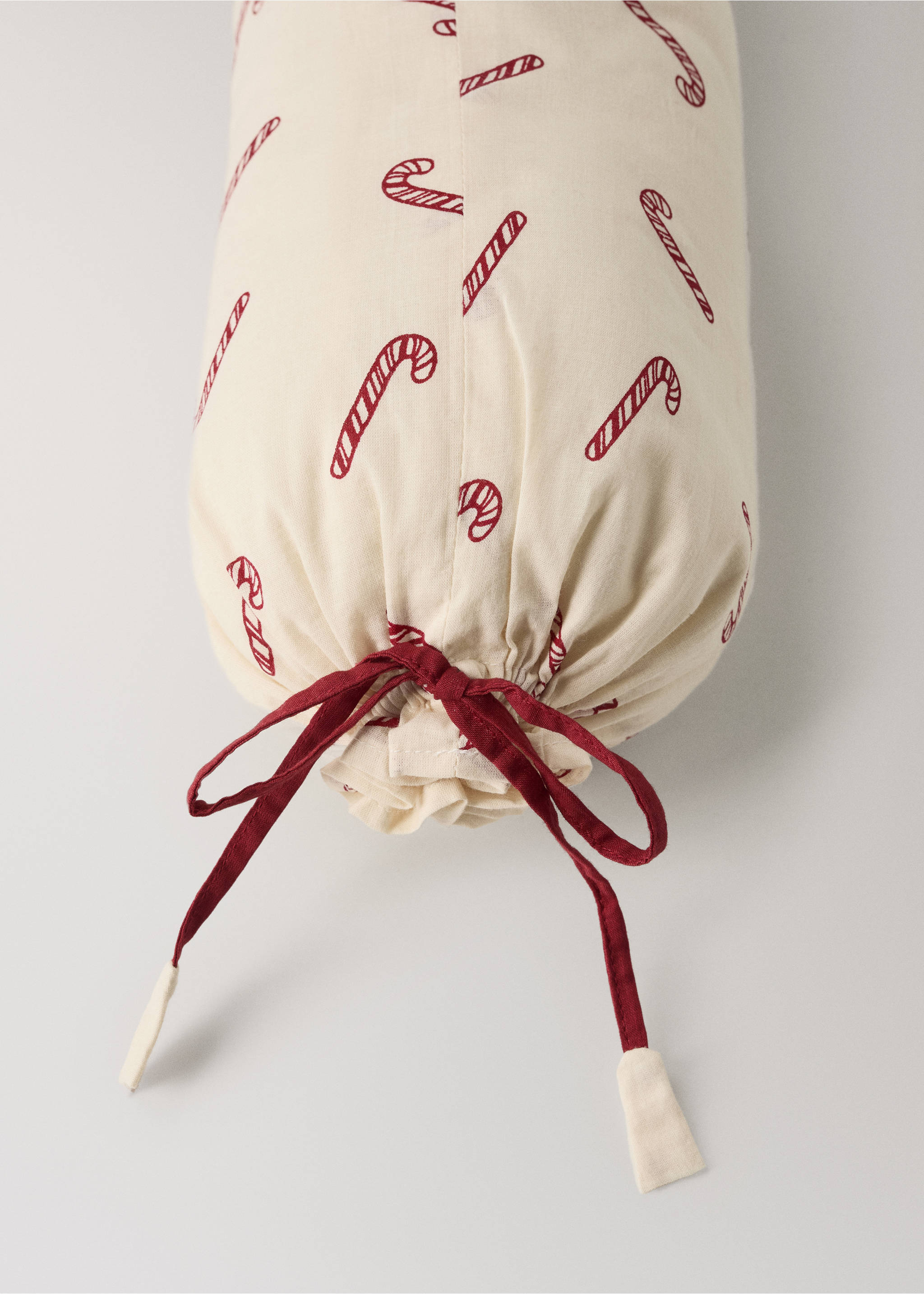 Cream cylindrical cushion with a red candy cane print and tie detail., Red. Ref: 37038636-00.