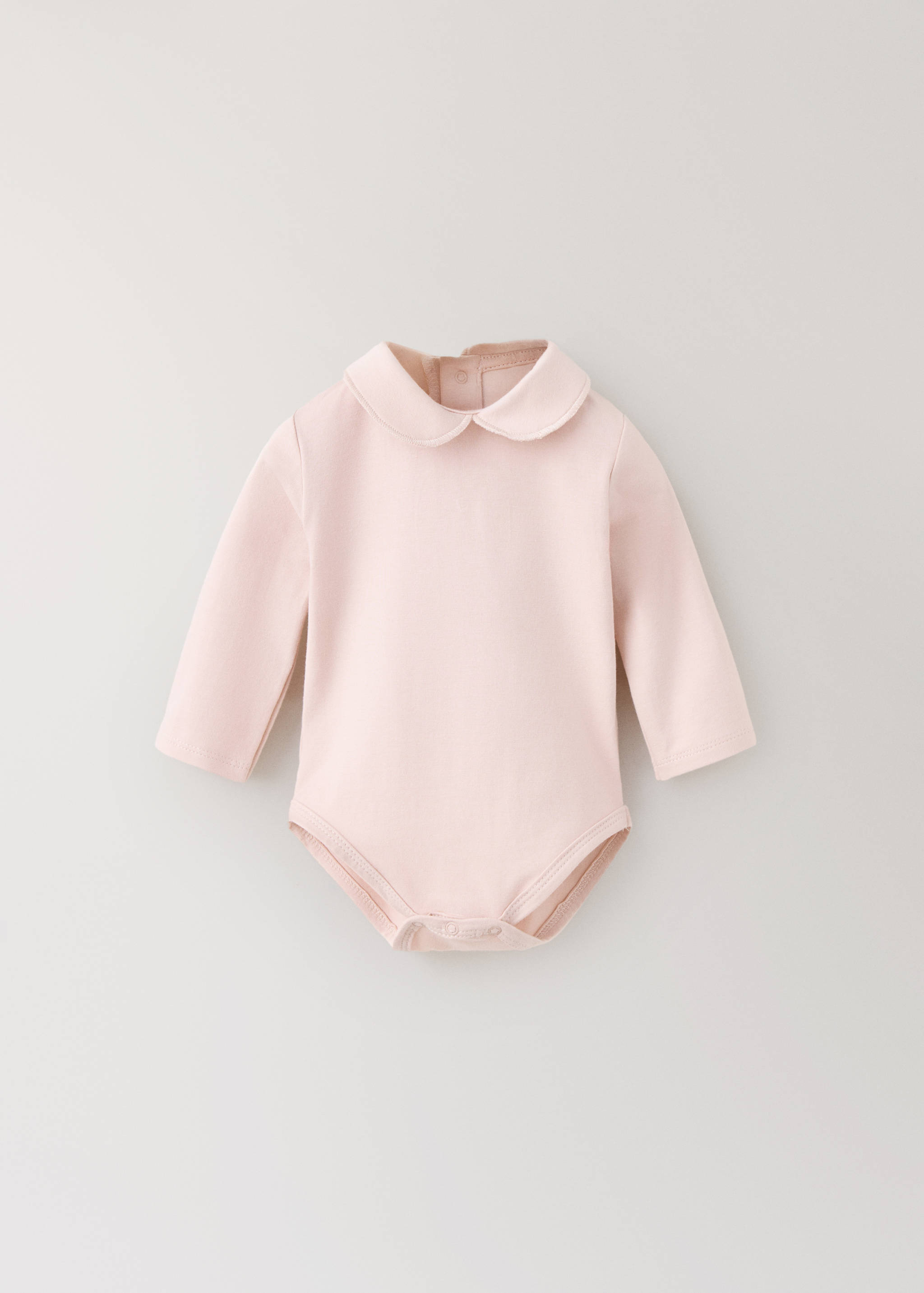 Pale pink baby bodysuit with long sleeves and Peter Pan collar.