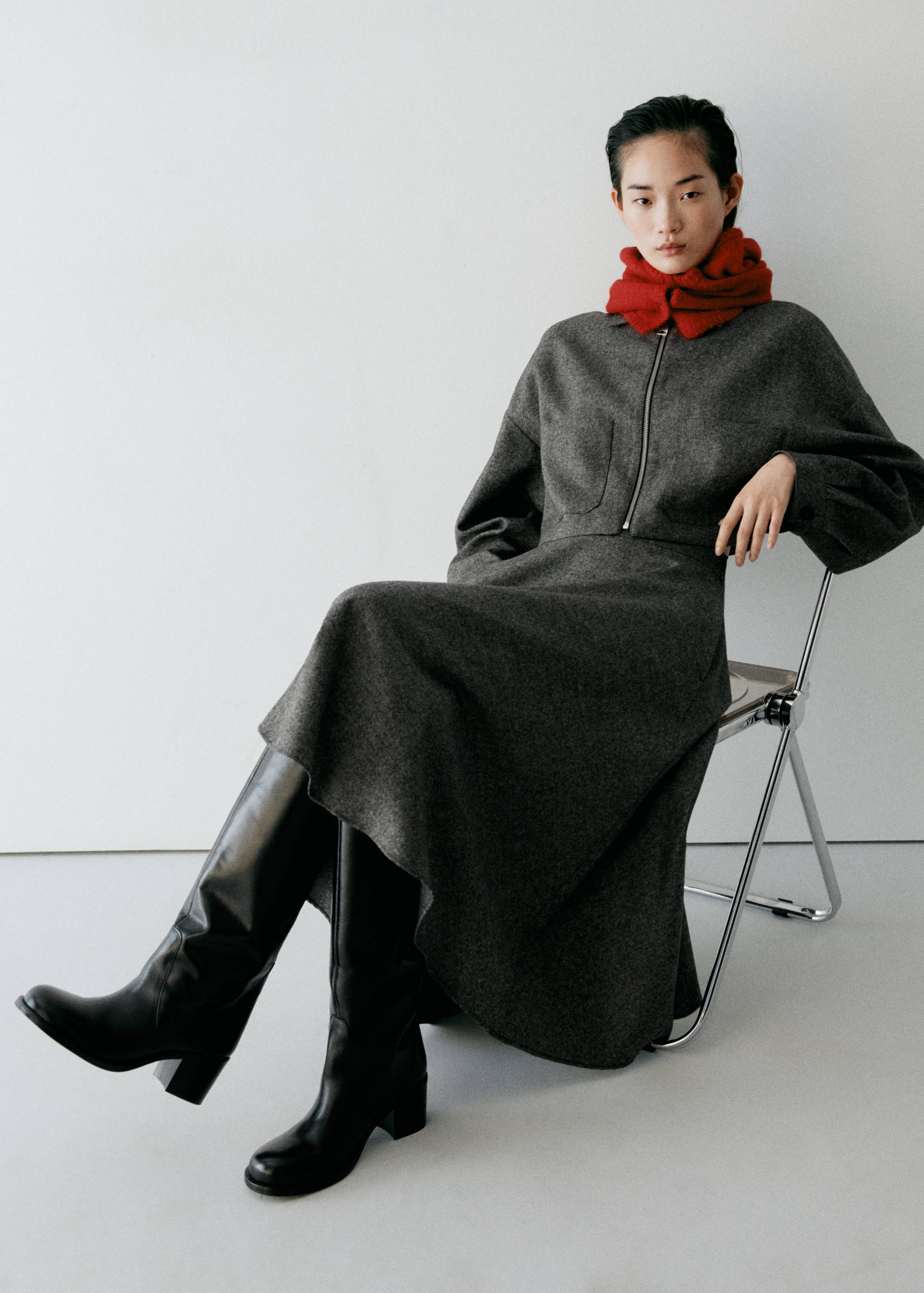 Dark grey zip-up jacket with collar and long sleeves, worn with a matching skirt and red scarf.