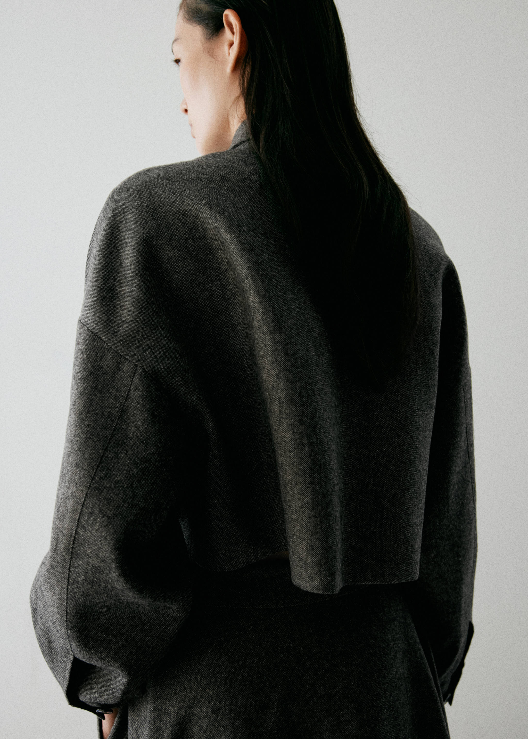 Dark grey cropped jacket shown from the back, featuring a high collar and dropped shoulders.