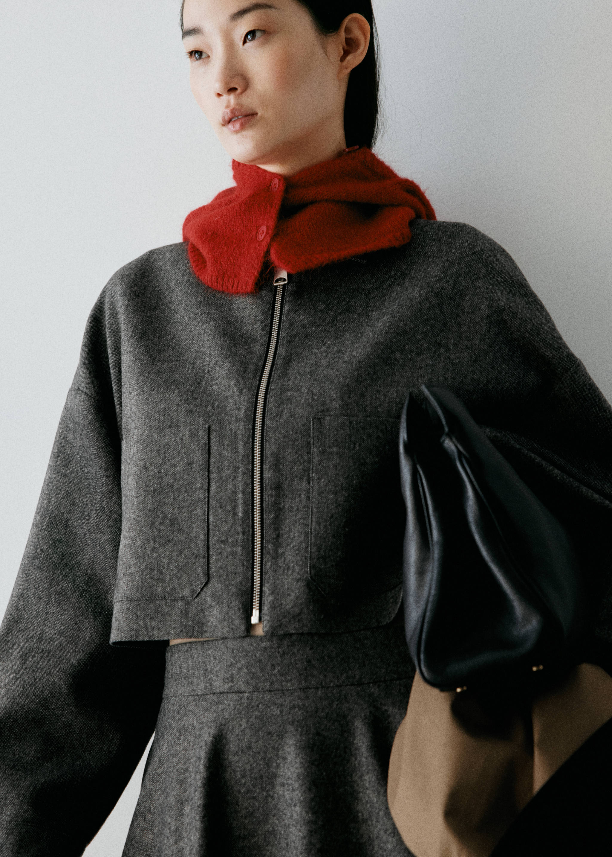Dark grey cropped zip jacket with patch pockets, worn with a red knitted scarf.