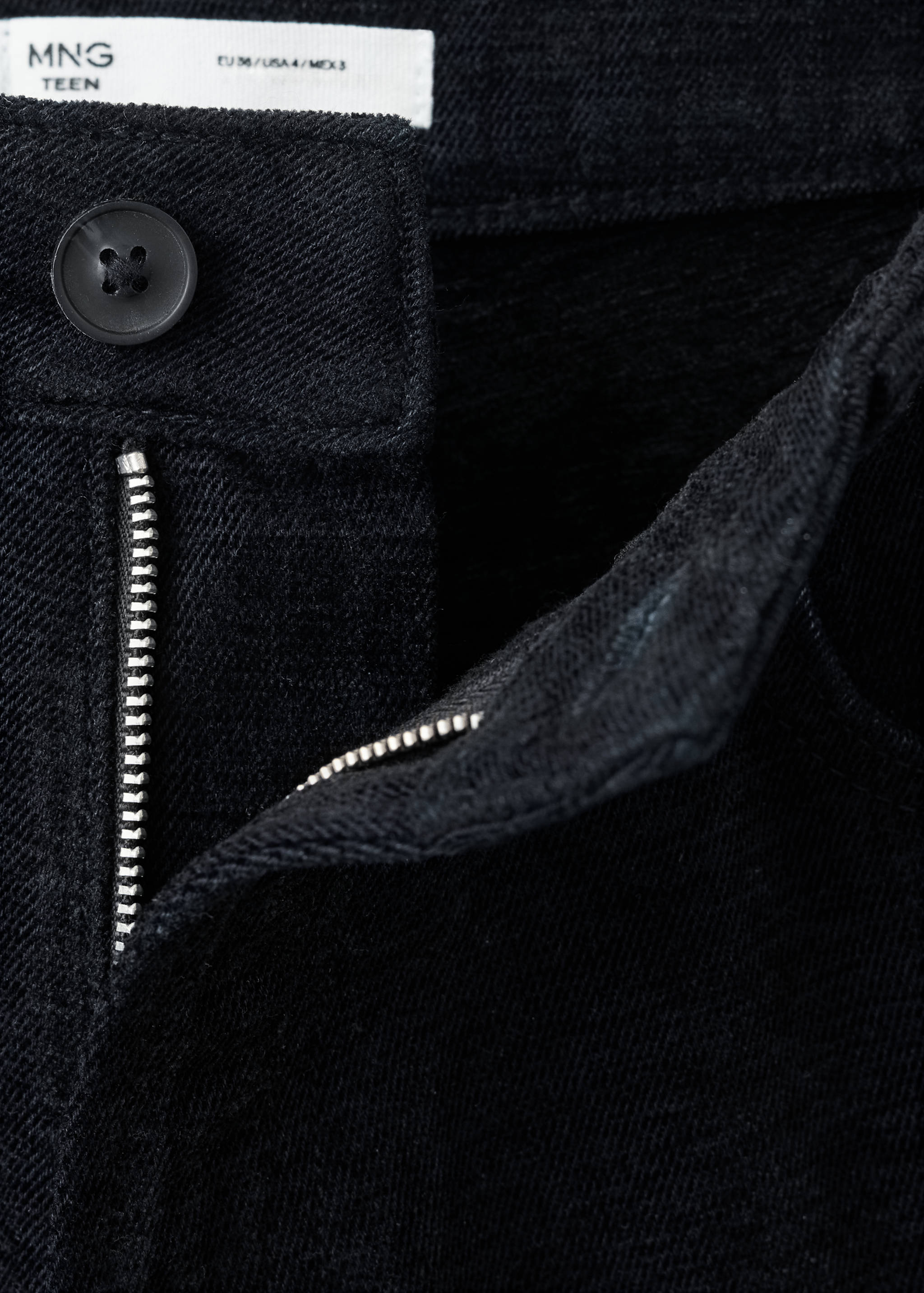 Close-up of black denim jeans waistband, zip fly and button.