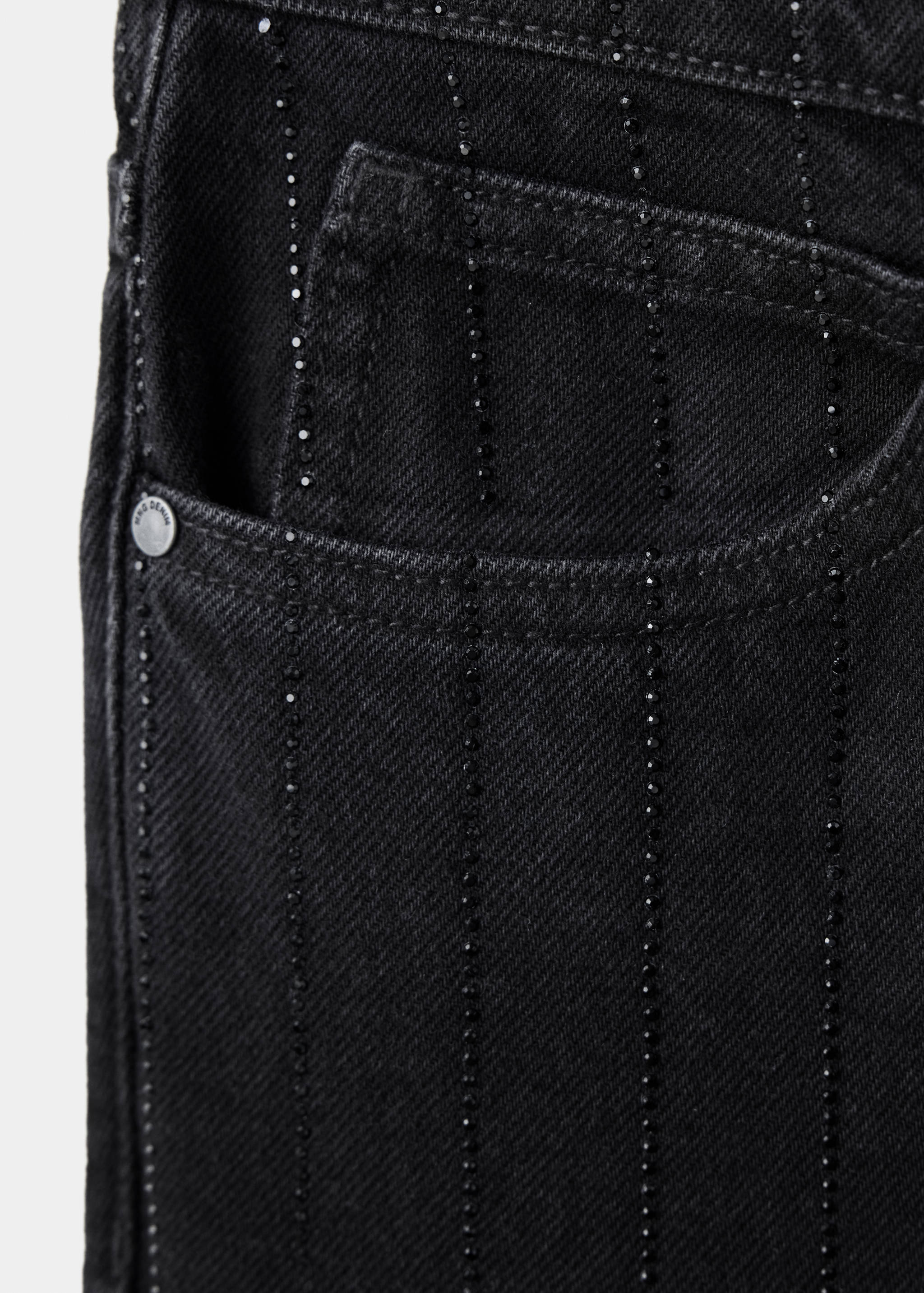 Primer plano del detalle de unos pantalones vaqueros negros con pedrería.