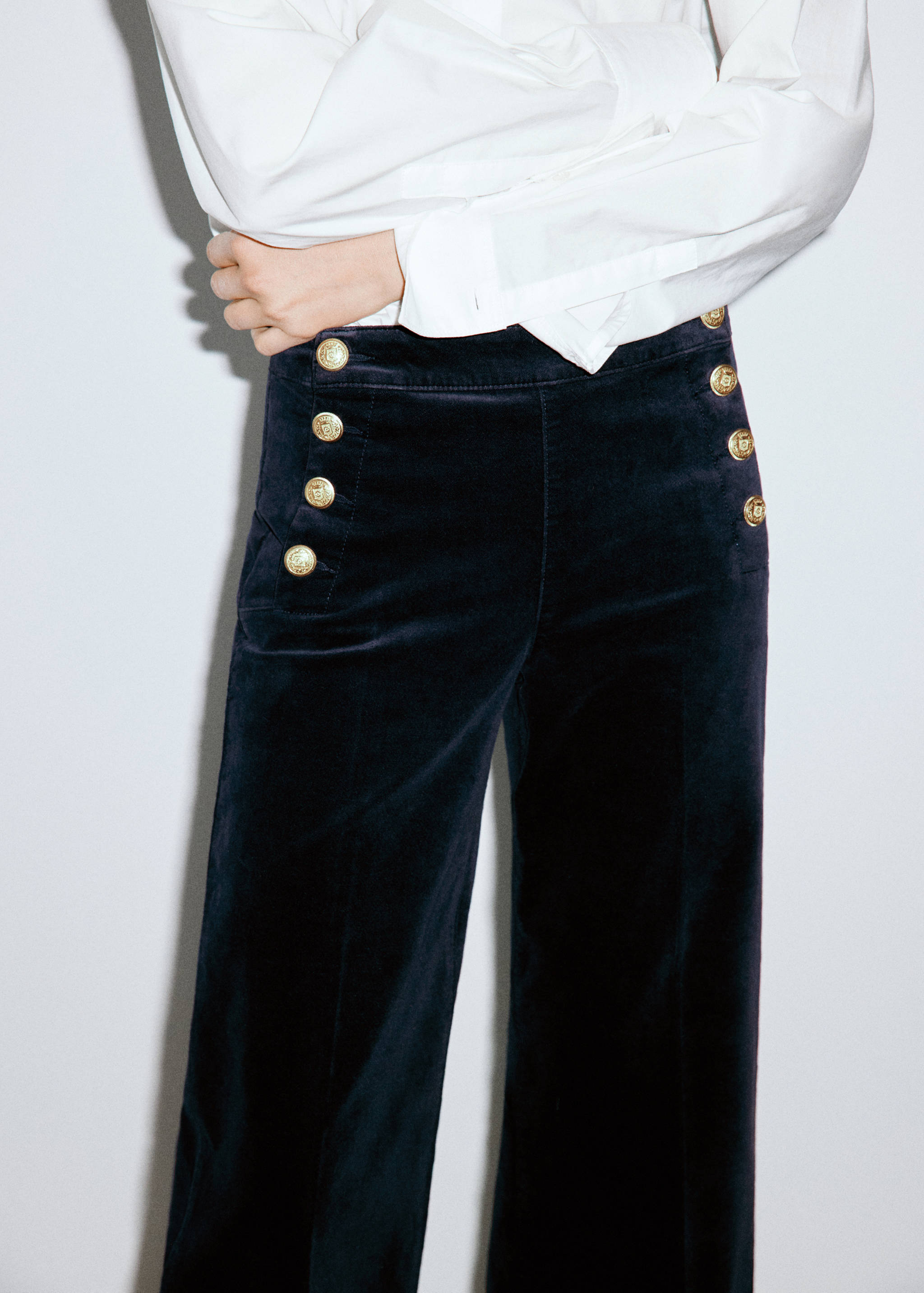 Dark blue velvet trousers with gold-tone decorative buttons worn with a white shirt.
