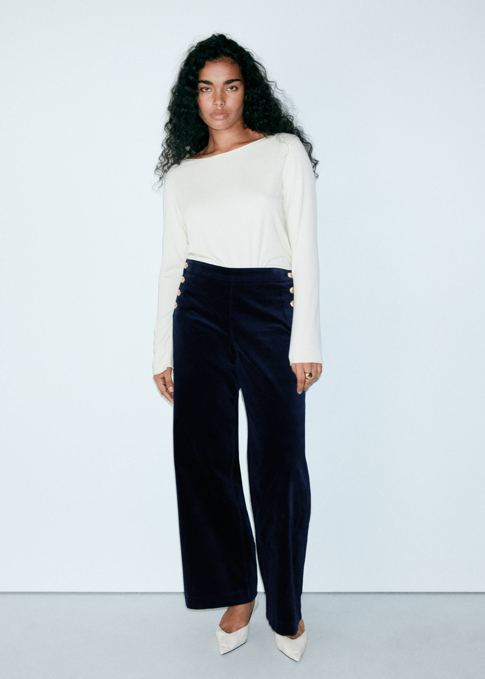 Dark navy blue wide-leg trousers with gold-toned side buttons, worn with a cream long-sleeved top.