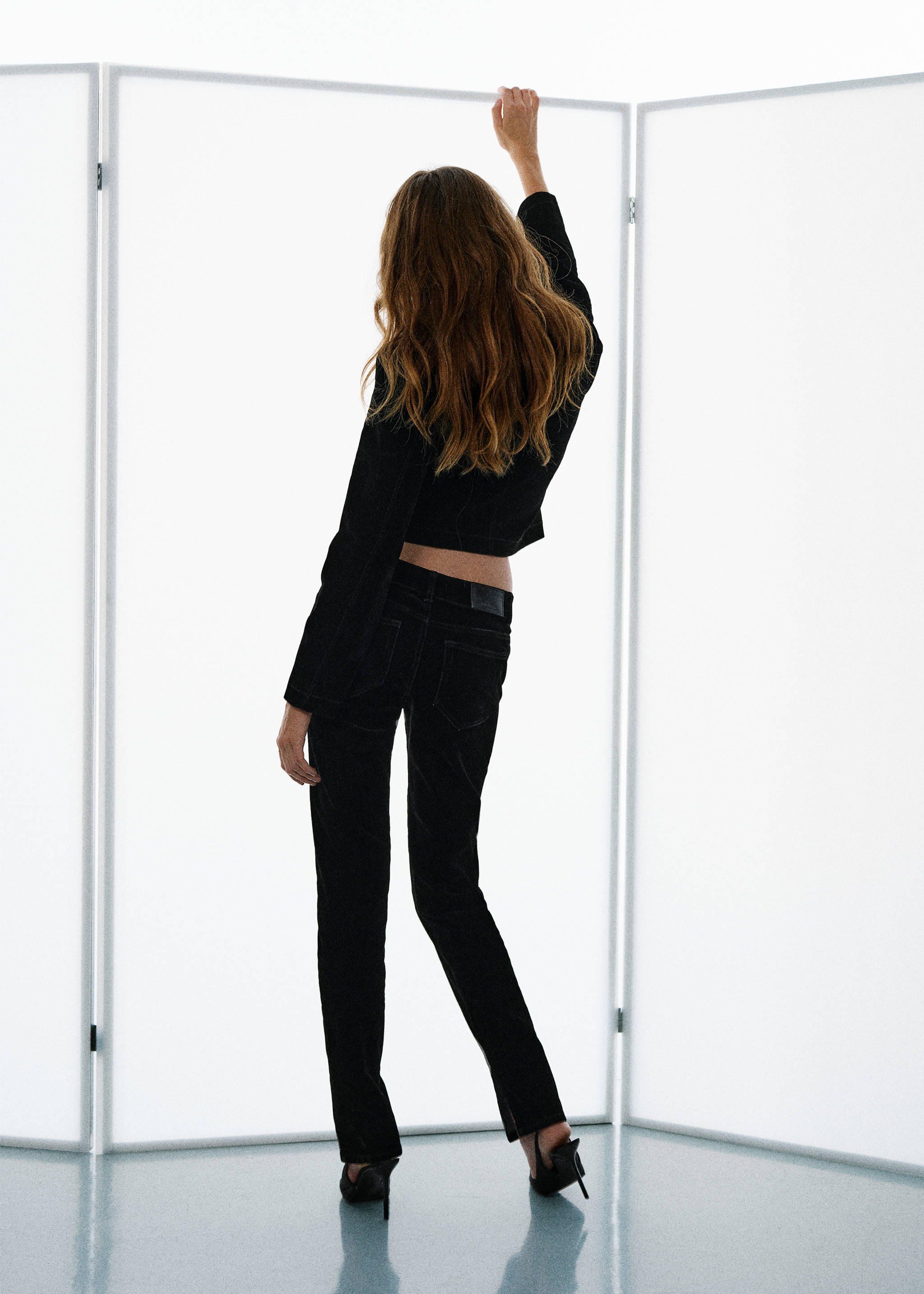 Back view of black denim trousers worn with a matching dark jacket.
