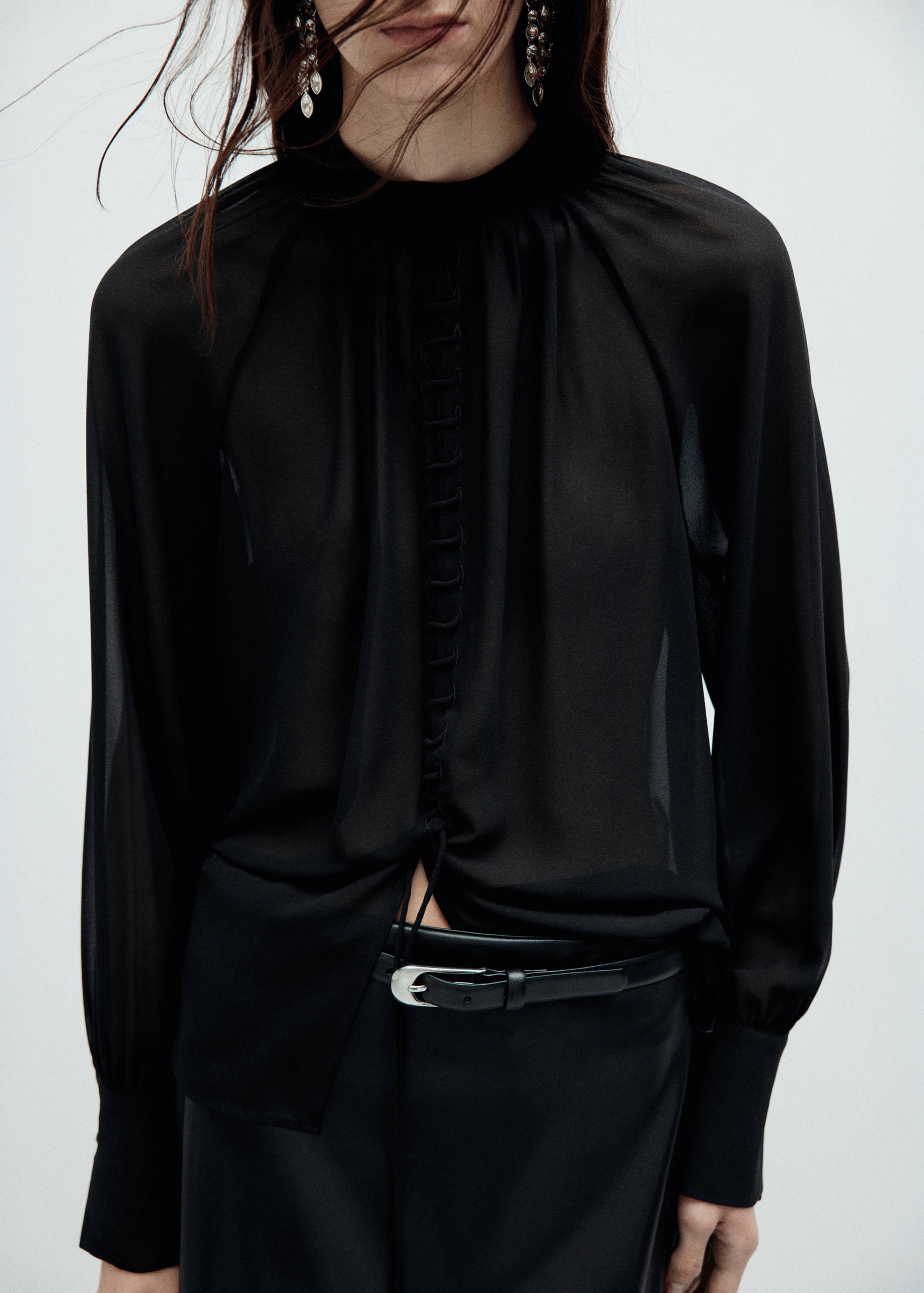 Blusa negra transparente de cuello alto, manga larga y detalle de botones en la parte delantera.