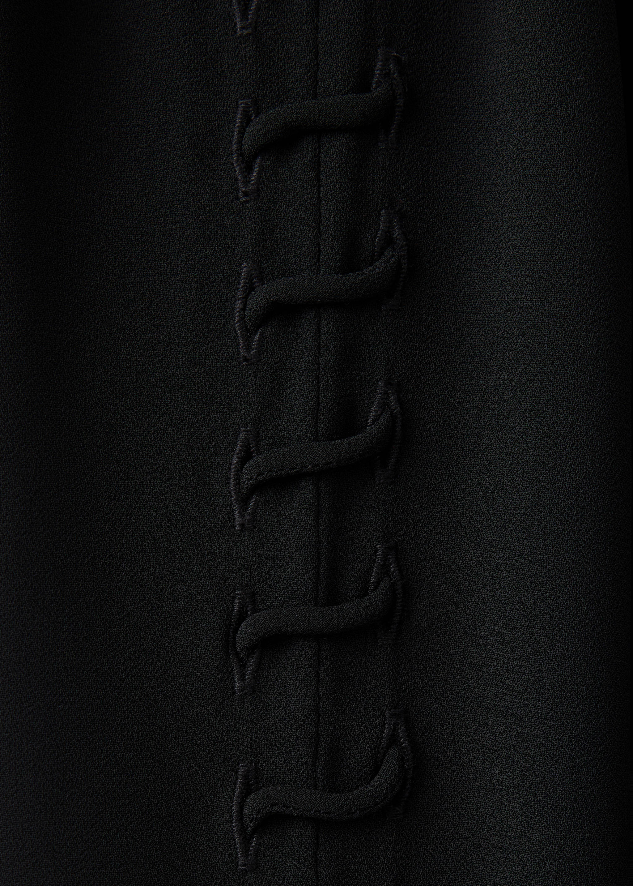 Detalle de la blusa negra con costura vertical y cordones de presilla.