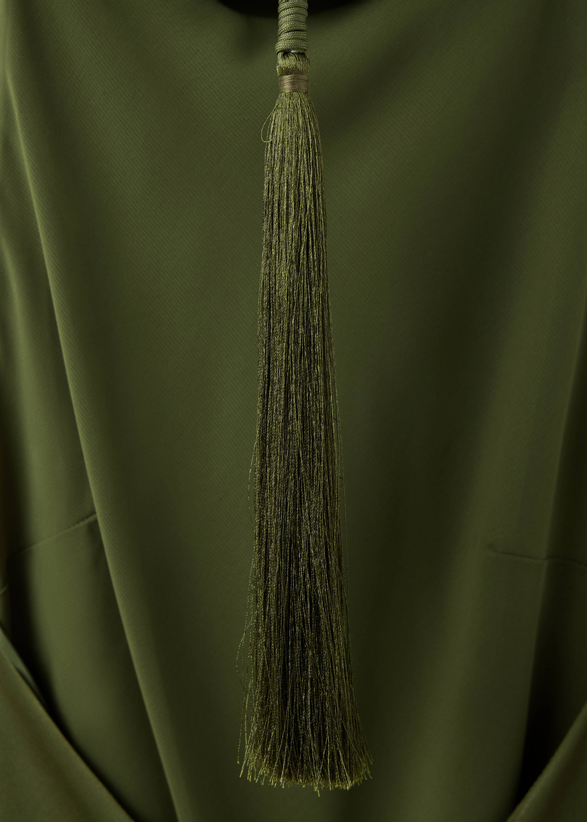 Detalle del tejido de vestido verde oliva con borla decorativa.