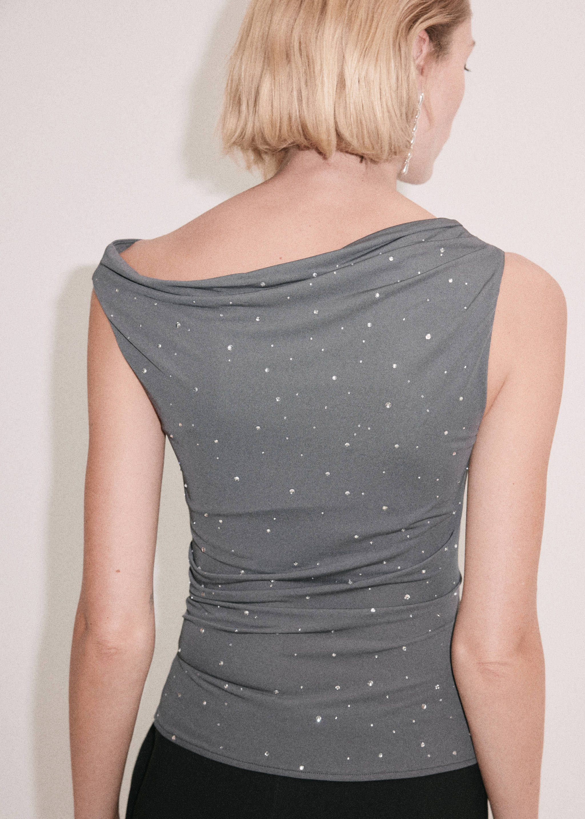 Back view of a grey sleeveless top with rhinestones and an asymmetrical draped neckline.