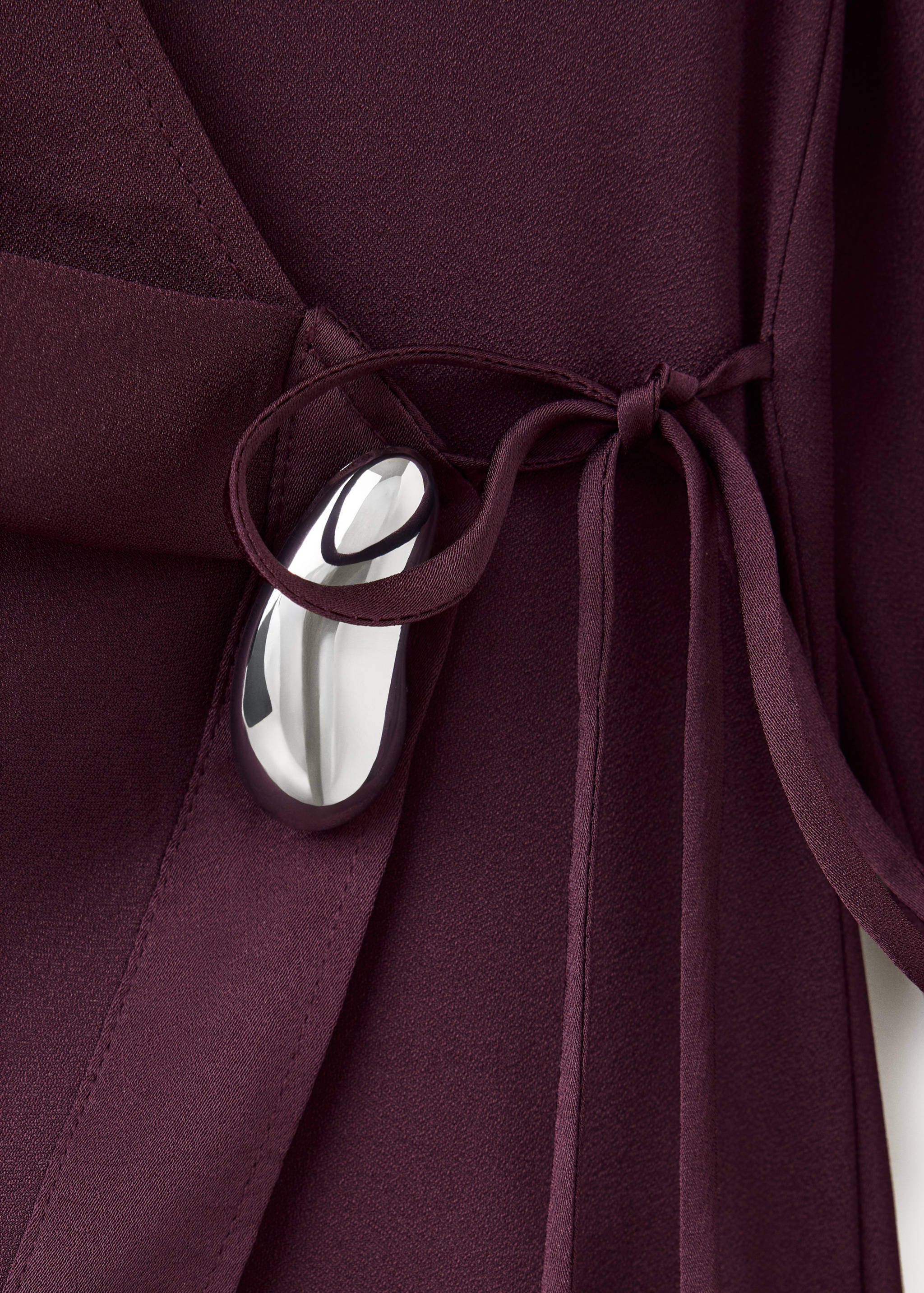 Burgundy shirt fabric detail with a wrap tie and metallic silver buckle.