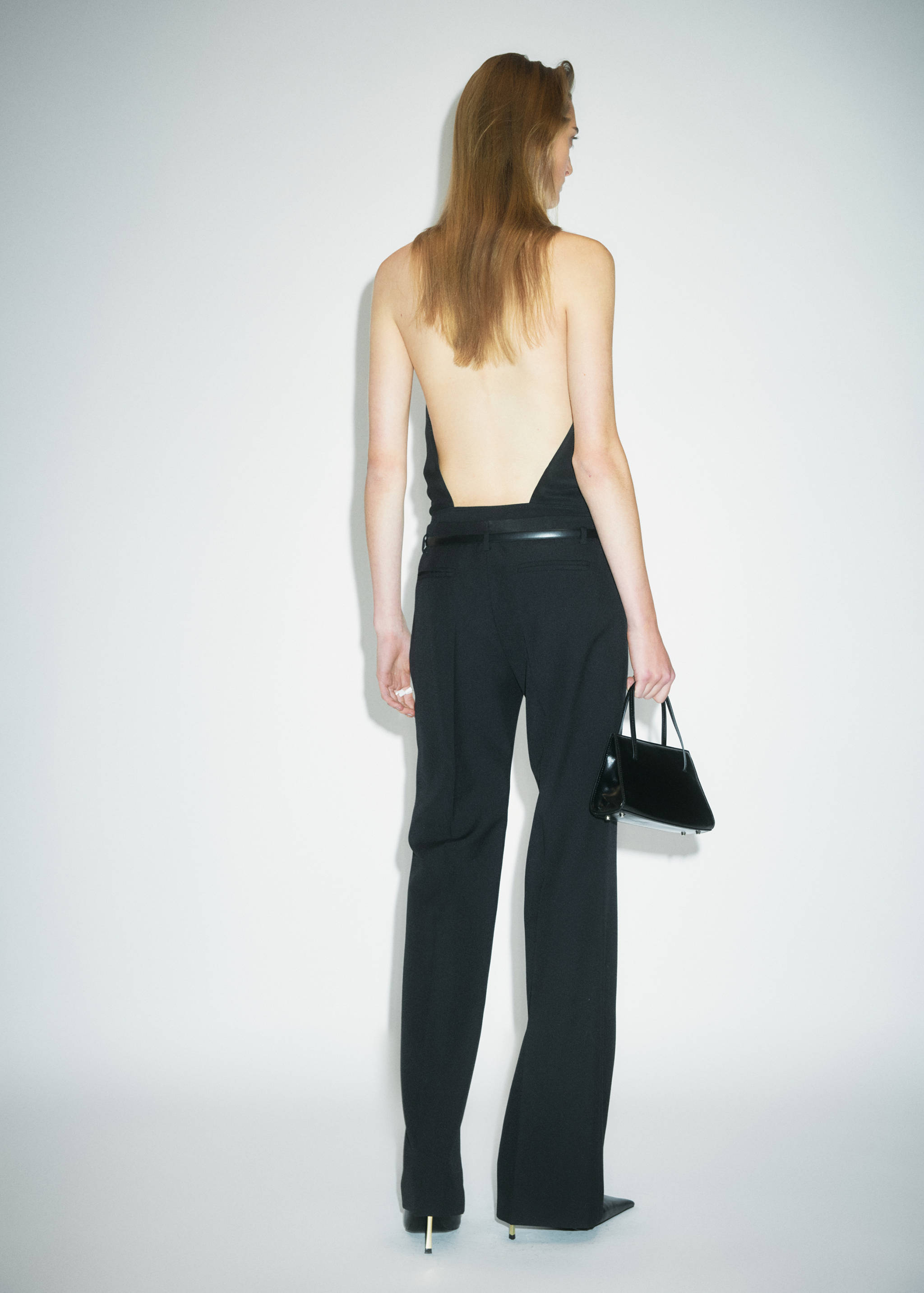 Back view of black trousers with a straight fit, worn with a matching top and thin belt.