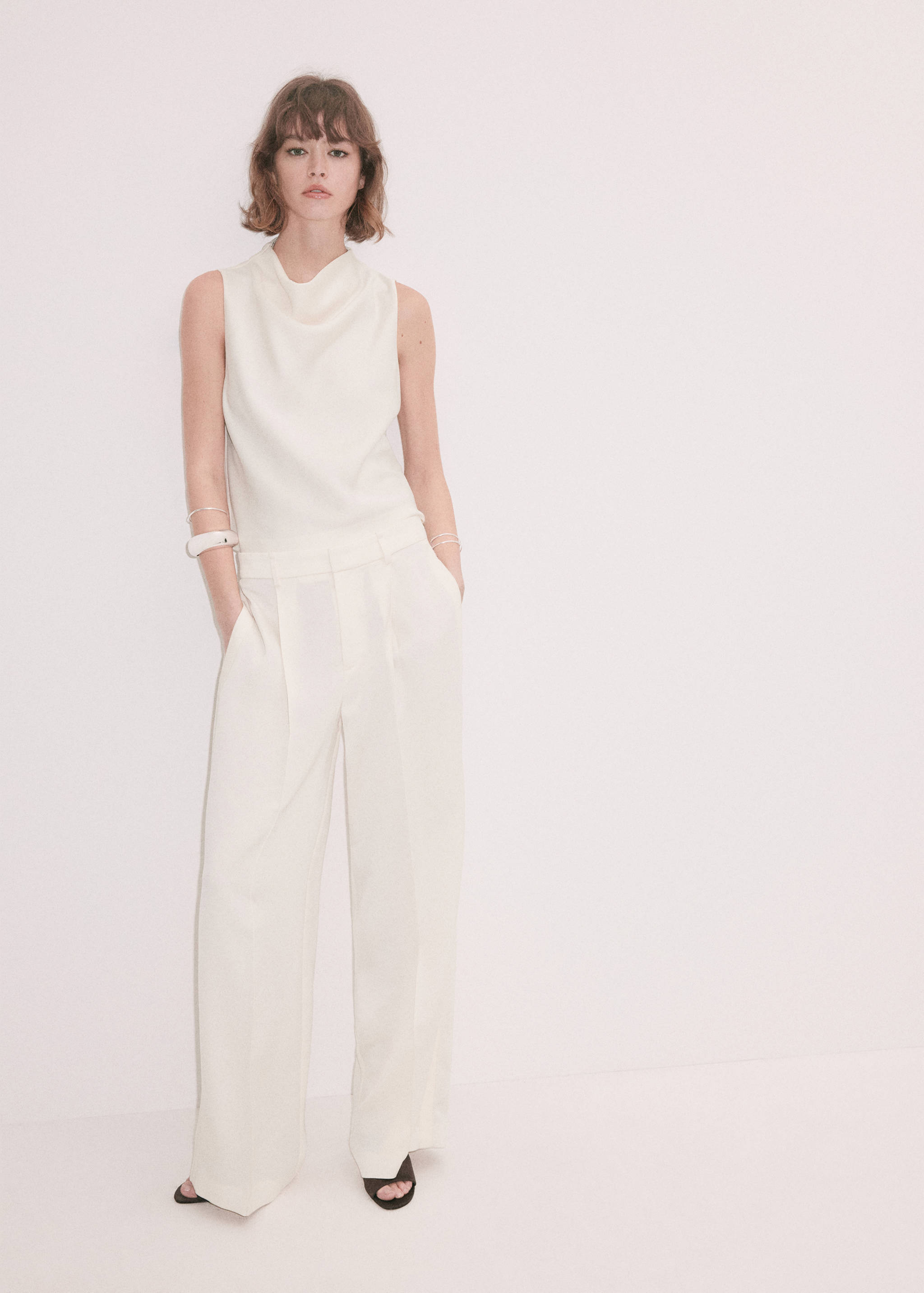 Off-white sleeveless top with a cowl neck, worn with matching wide-leg trousers.