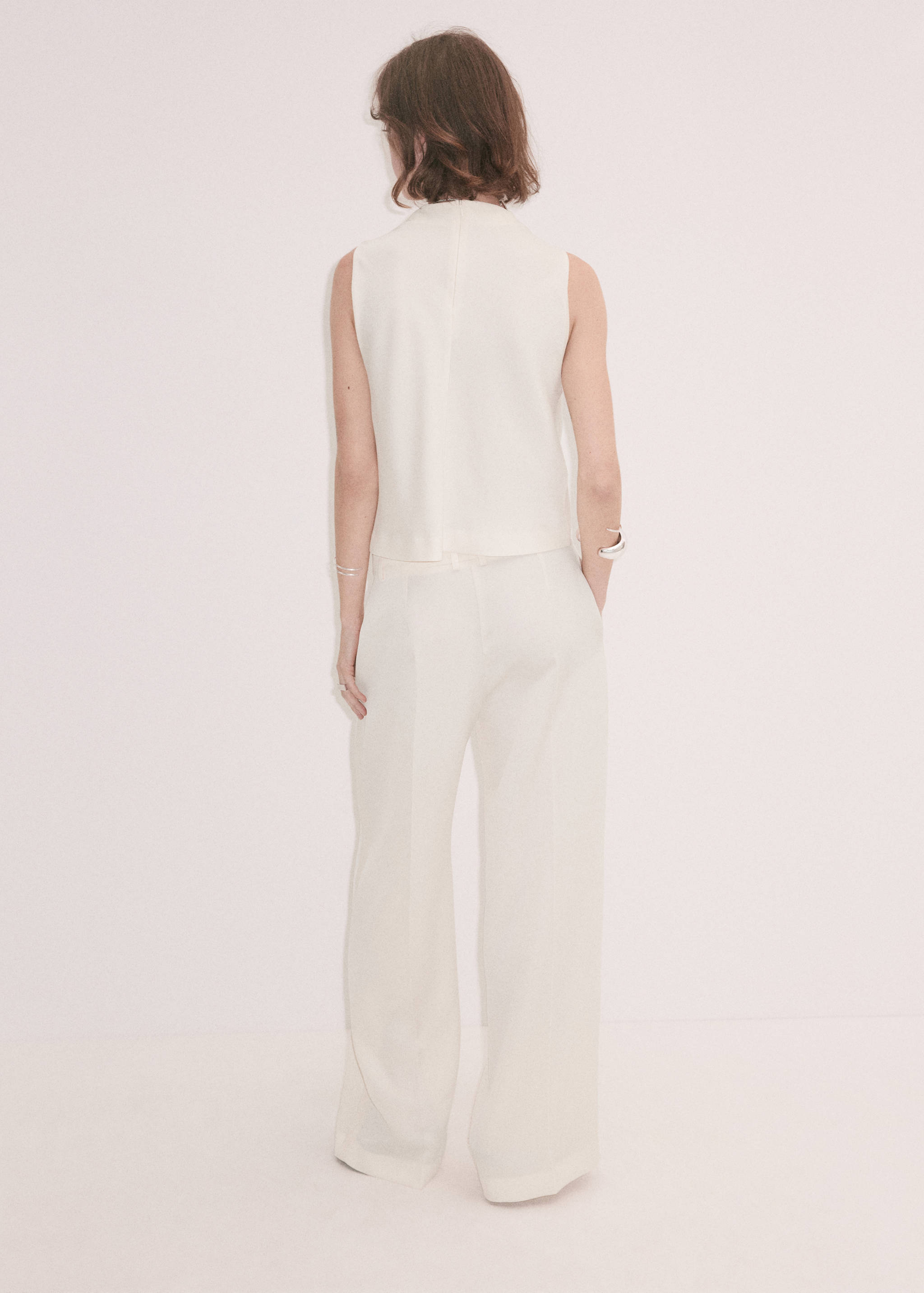 Cream sleeveless top shown from the back, paired with trousers