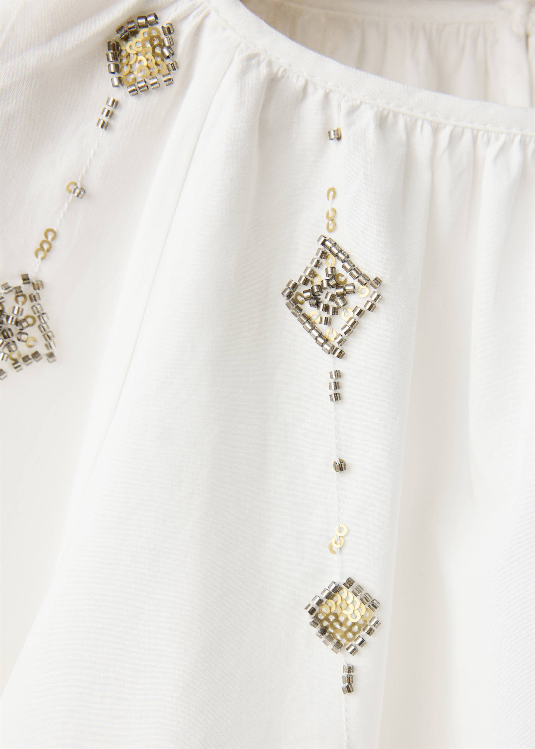 Close-up of a white blouse with beaded and sequinned diamond embroidery.
