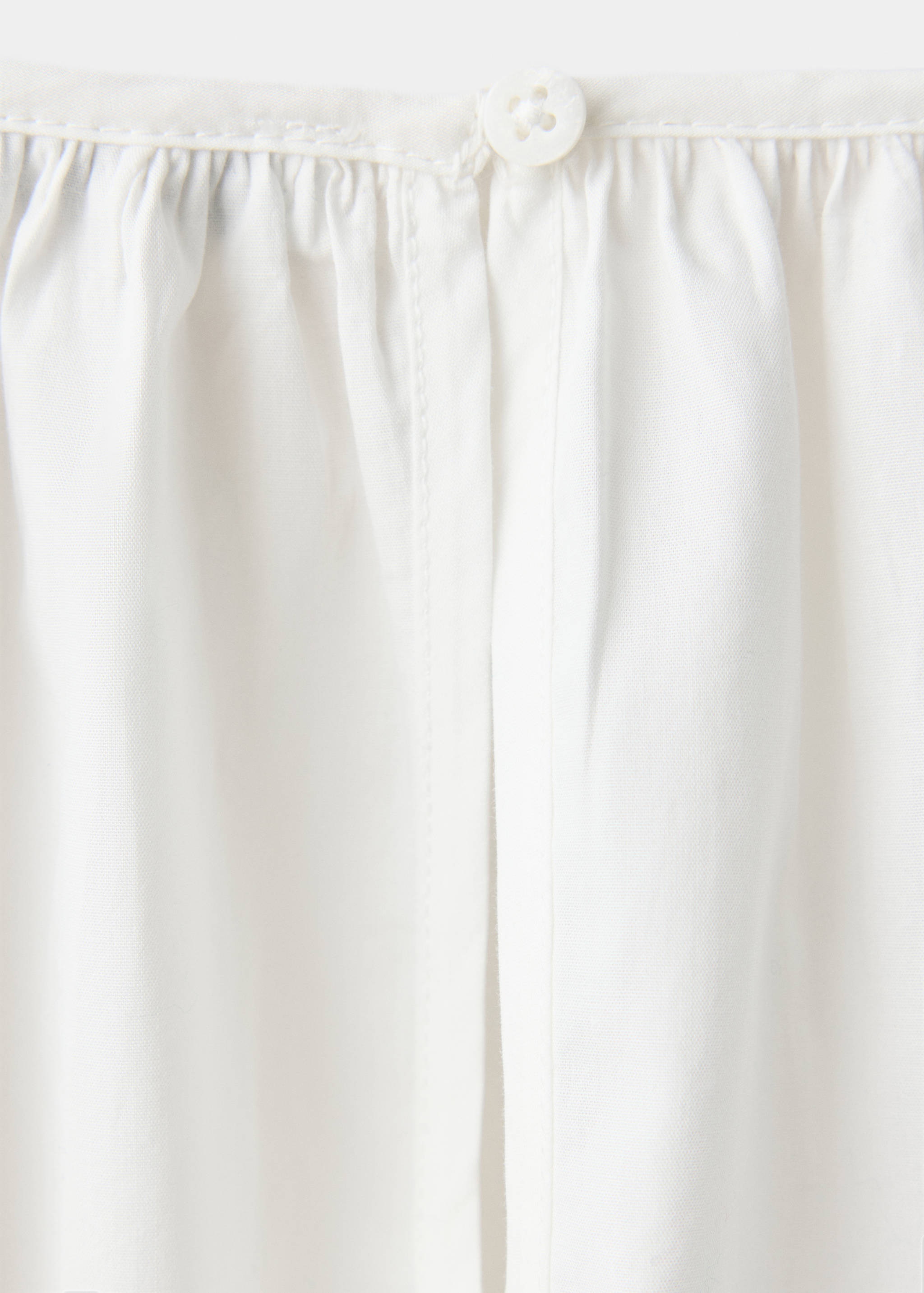 Close-up of white children's blouse fabric with gathered neckline and button.