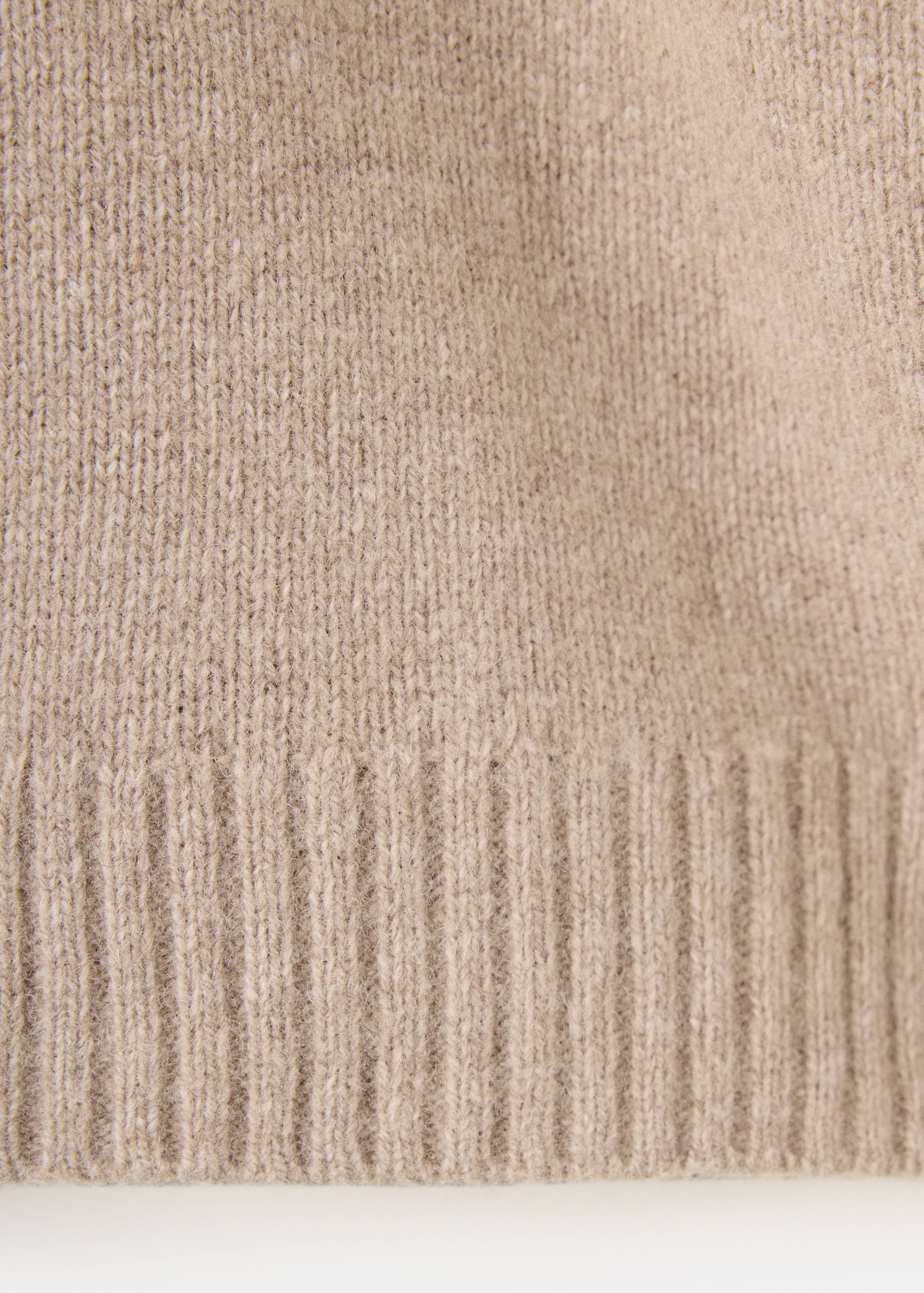 Close-up of a beige children's knitted sweater showing the ribbed hem.