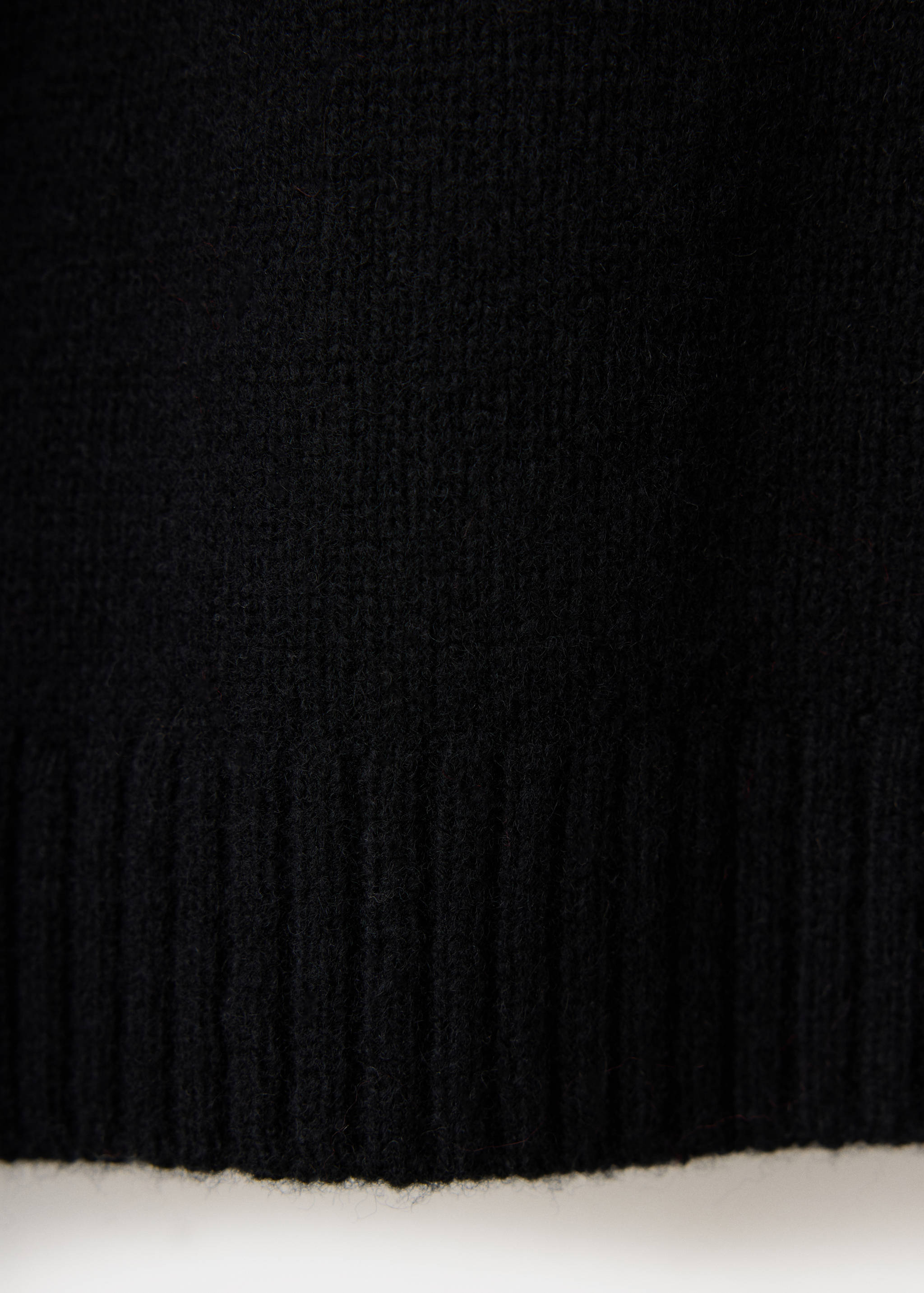 Close-up of the black knit fabric and ribbed hem of a sweater.