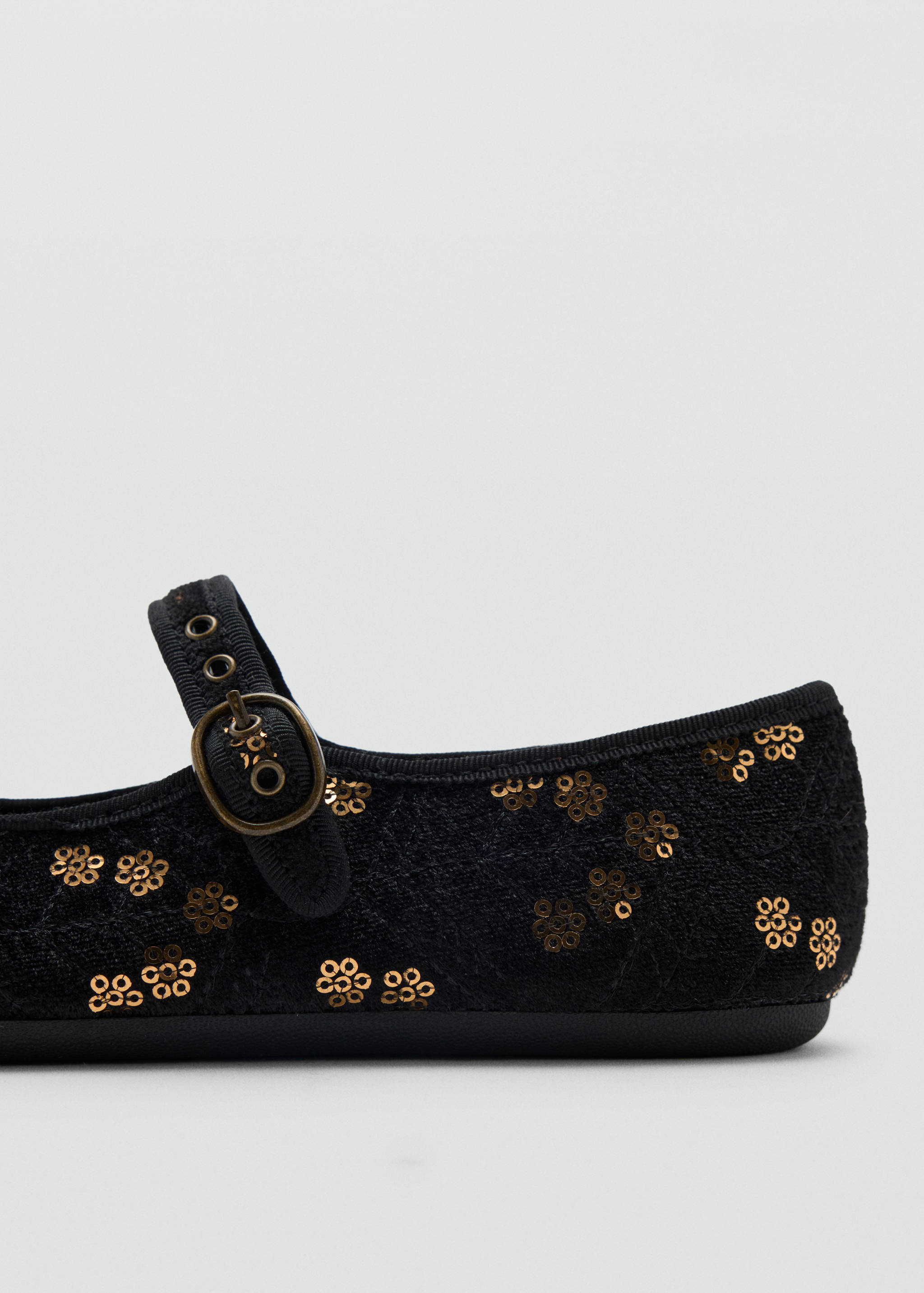 Close-up of a child's black shoe with bronze sequin flowers and a buckled strap.