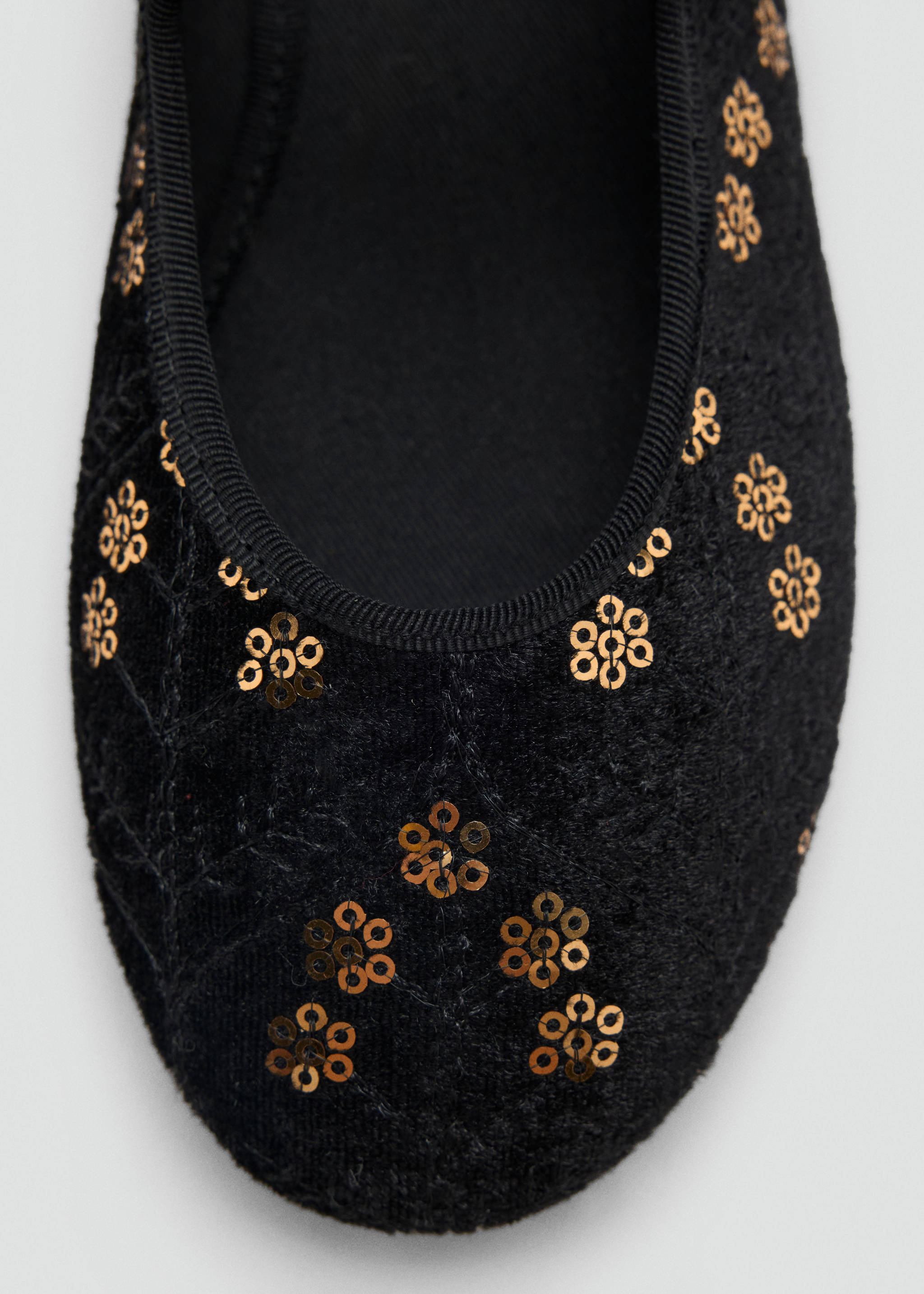 Close-up of a black shoe with gold sequin flower details and grosgrain trim.