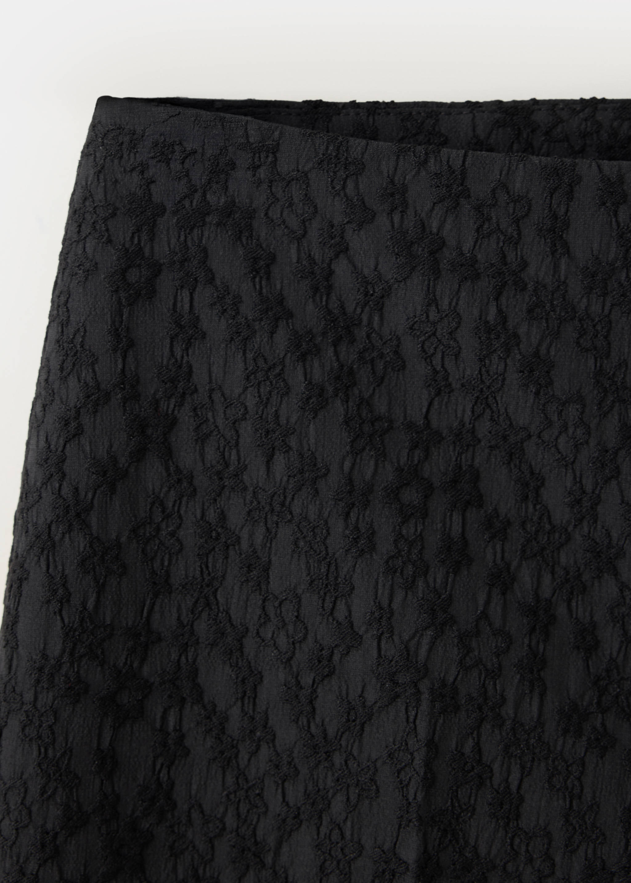 Close-up of black trousers featuring a textured floral lace fabric.