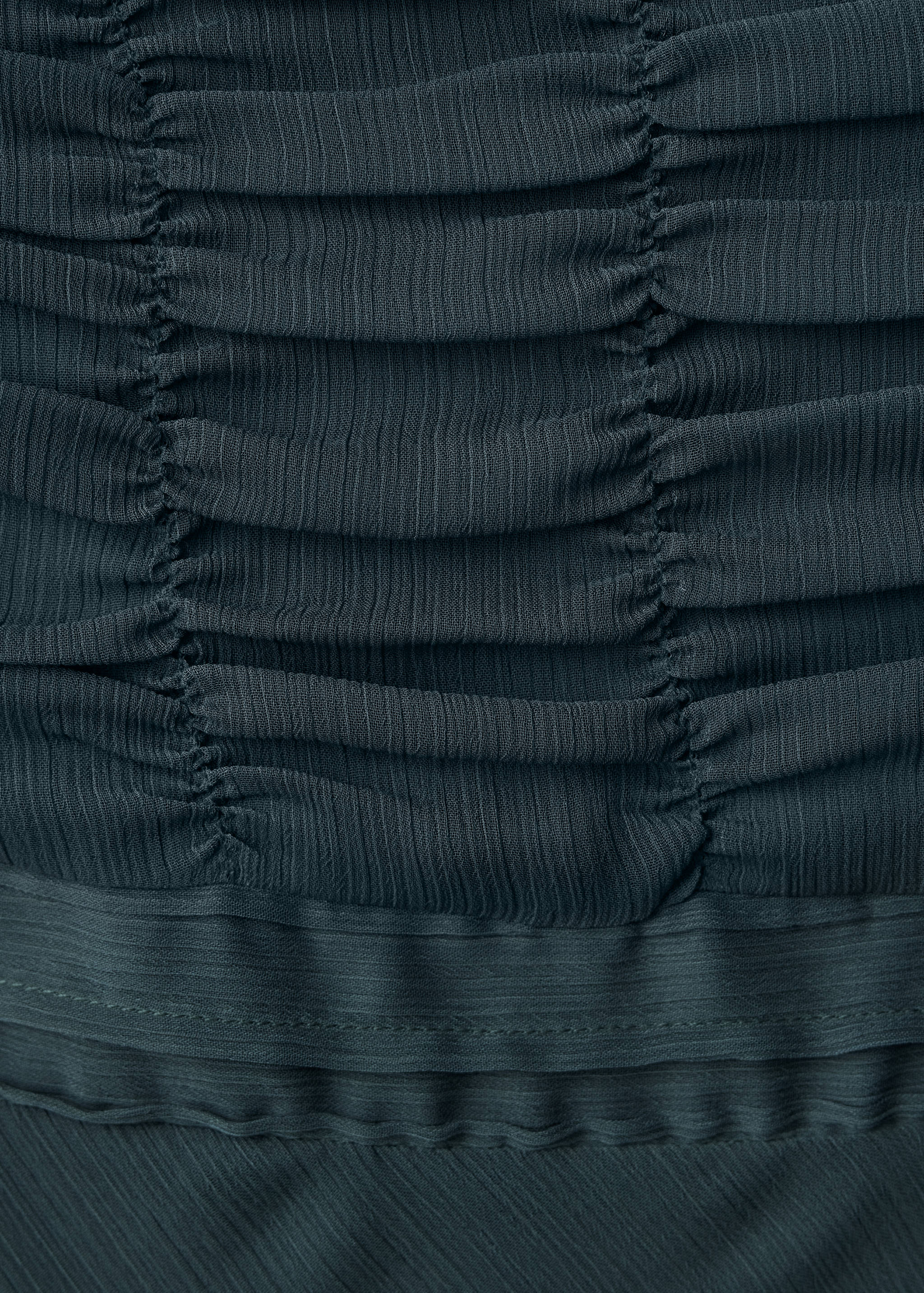 Close-up of the dark teal dress featuring pleated fabric and horizontal ruching.